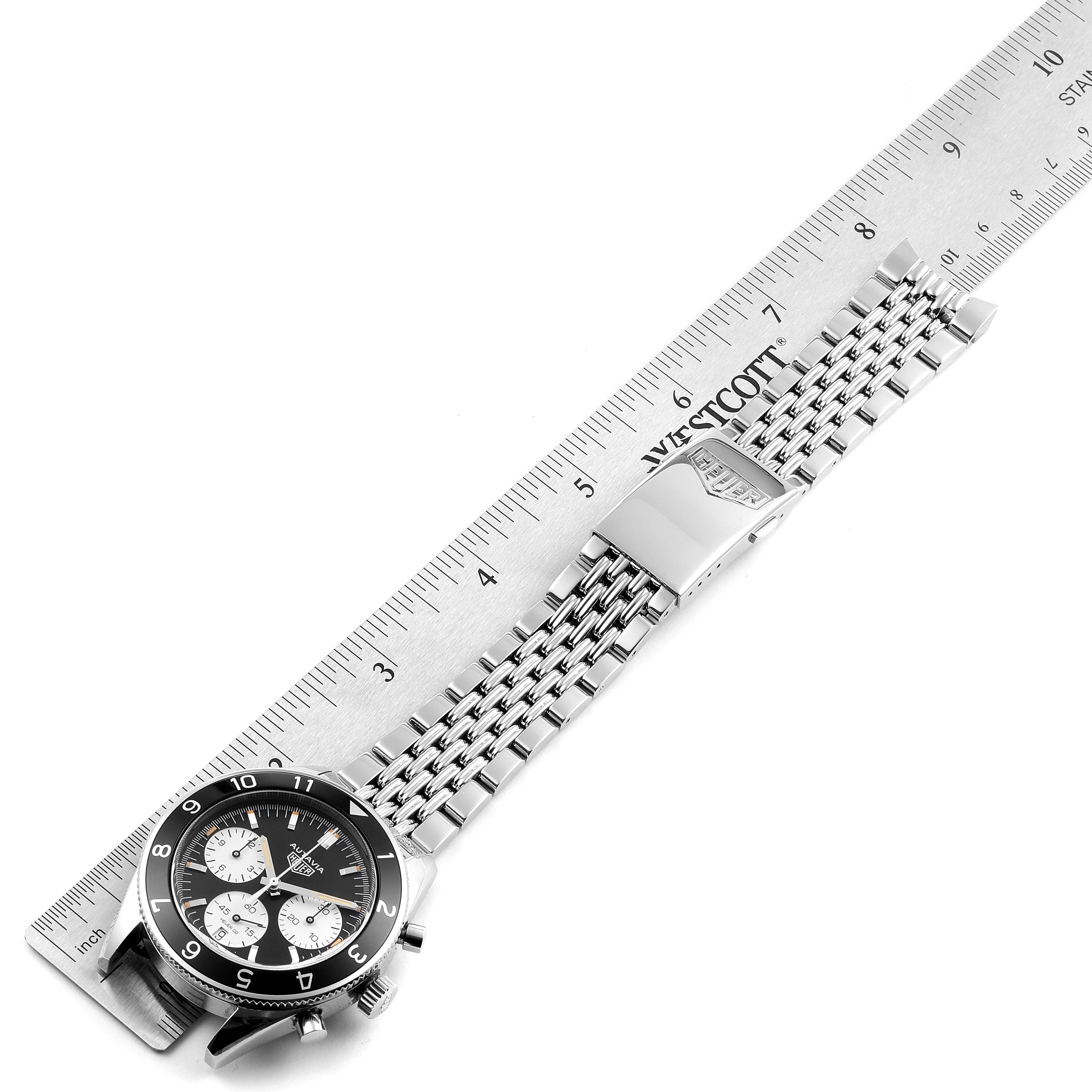 The image shows an overhead view of a Tag Heuer Autavia CBE2110.BA0687 Men's Stainless Steel Black Dial CBE2110.BA0687 Men's Stainless Steel Black Dial model watch with its stainless steel bracelet laid next to a ruler.