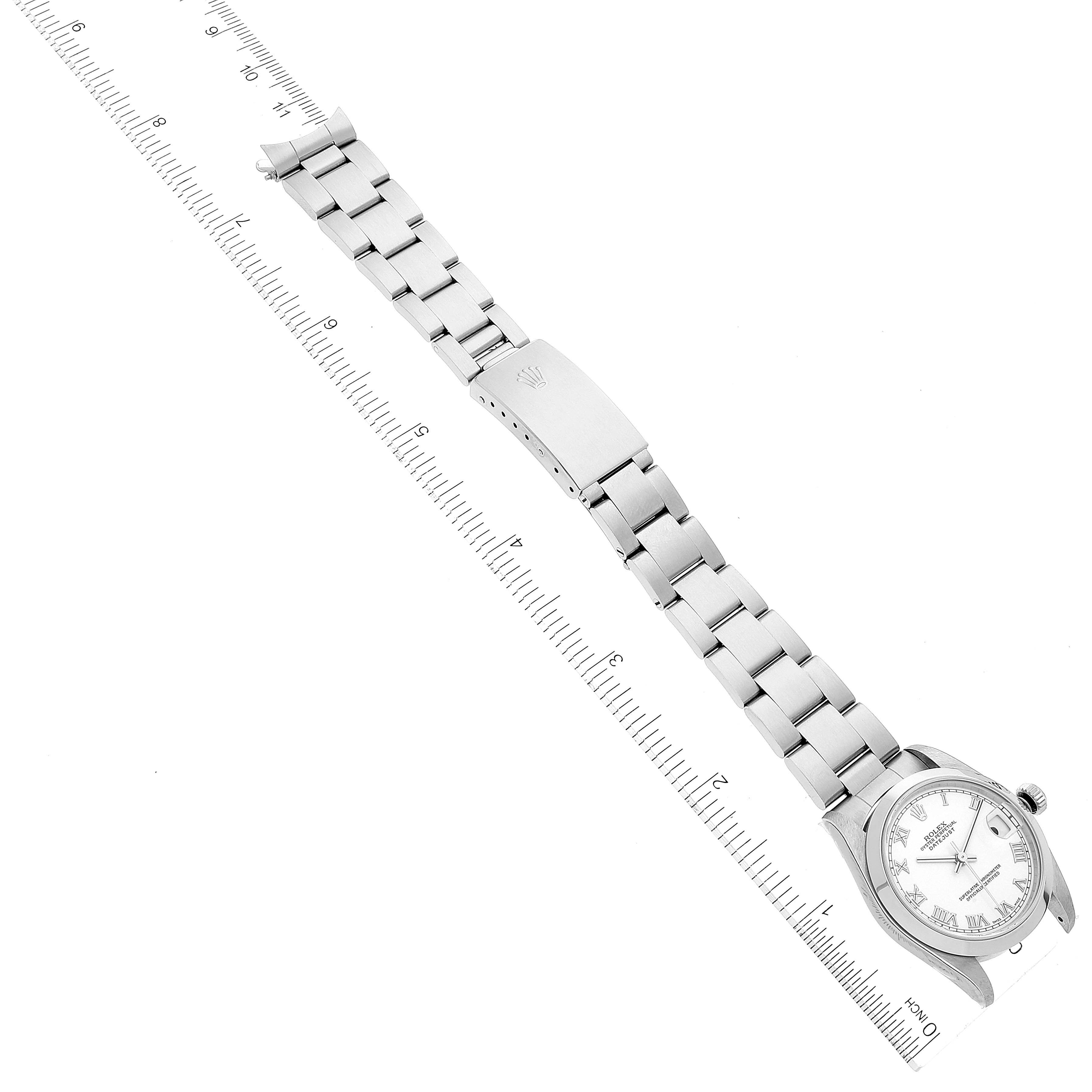The image shows an overhead view of a Rolex Mid-Size 78240 Women
s Stainless Steel White Dial 78240 Women
s Stainless Steel White Dial watch, including the face, bracelet, and clasp, alongside a ruler for scale.