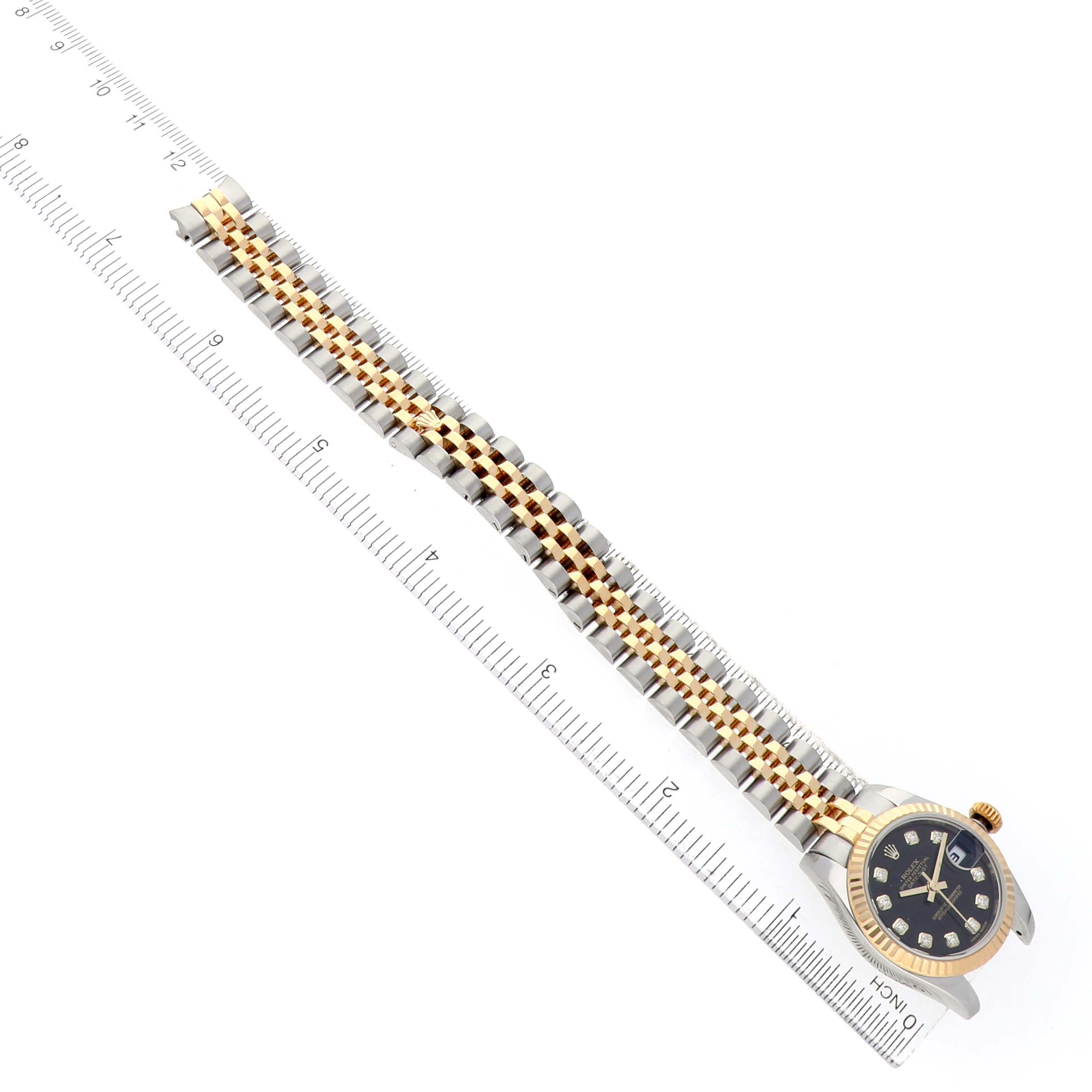 The image shows a Rolex Datejust 179173 Women's Steel and Gold (two tone) Black Dial watch from the top, highlighting its two-tone bracelet and bezel alongside a ruler for scale.