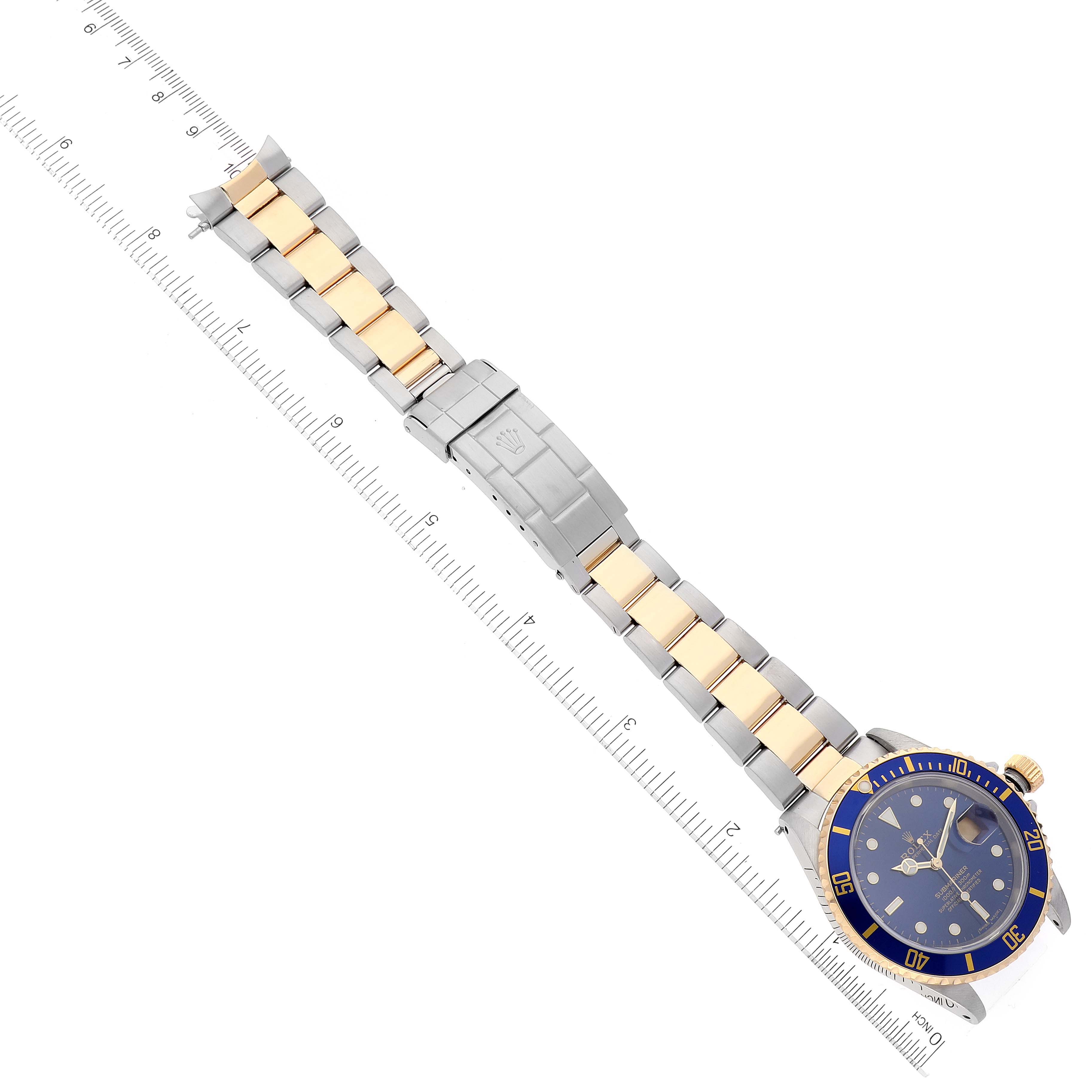 The image shows a Rolex Submariner 16613 Men's Steel and Gold (two tone) Blue Dial 16613 Men's Steel and Gold (two tone) Blue Dial watch laid flat with its face and bracelet fully visible, positioned next to a ruler.