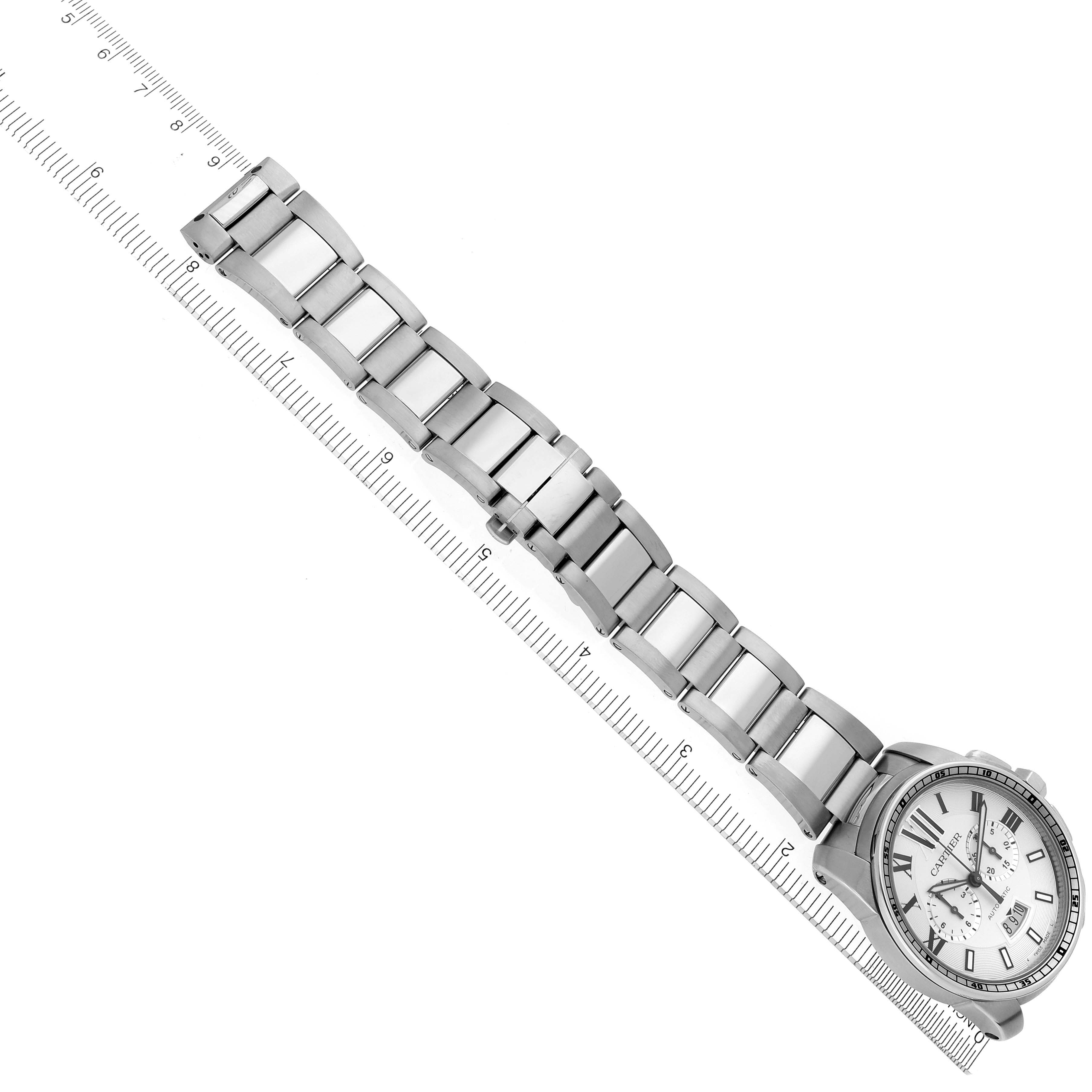 The image shows the Calibre de Cartier watch by Cartier at an angled top view, displaying the watch face and metal bracelet alongside a ruler.