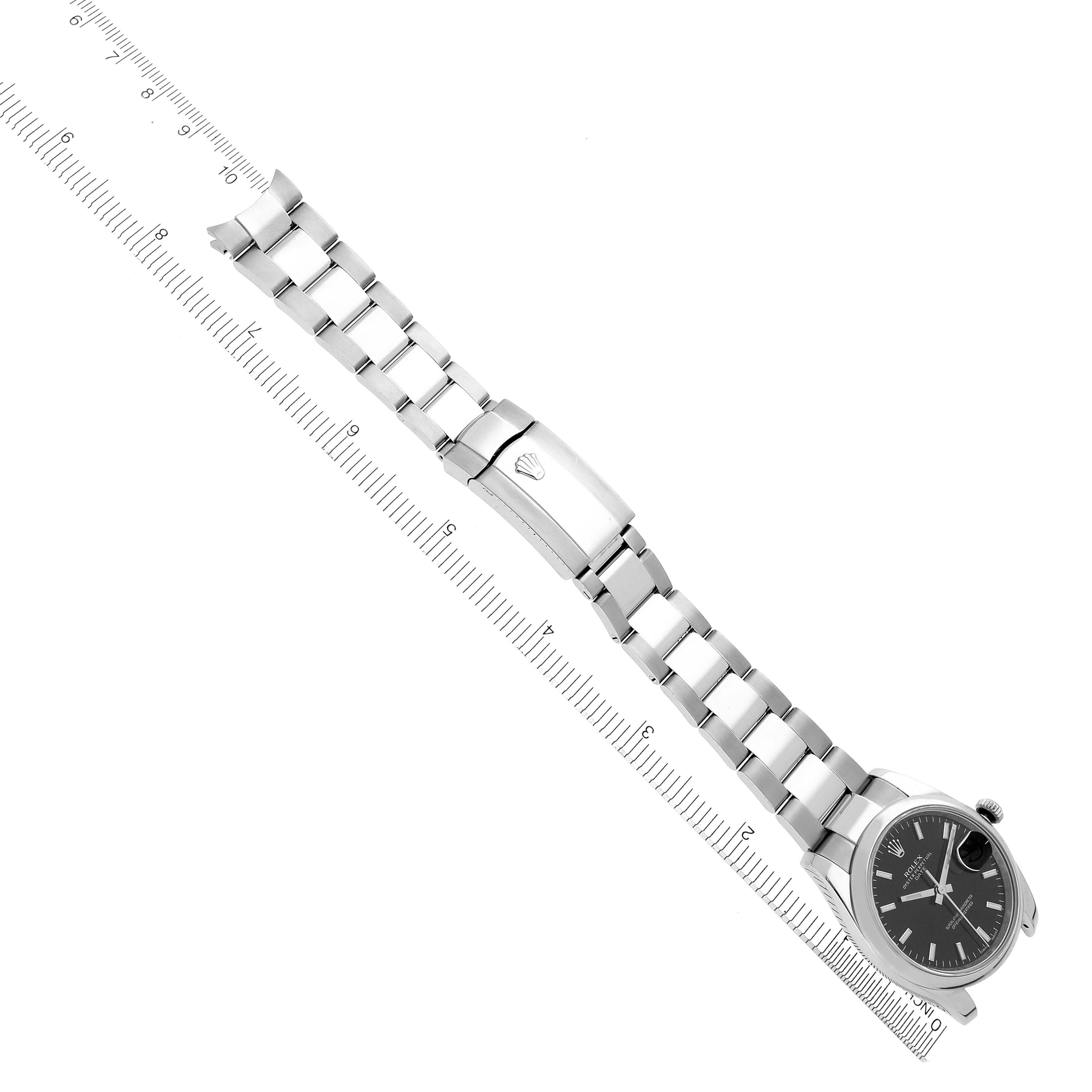The image shows a Rolex Date 115200 Men's Stainless Steel Black Dial 115200 Men's Stainless Steel Black Dial model watch from an angled view, highlighting the face and the full bracelet alongside a ruler.