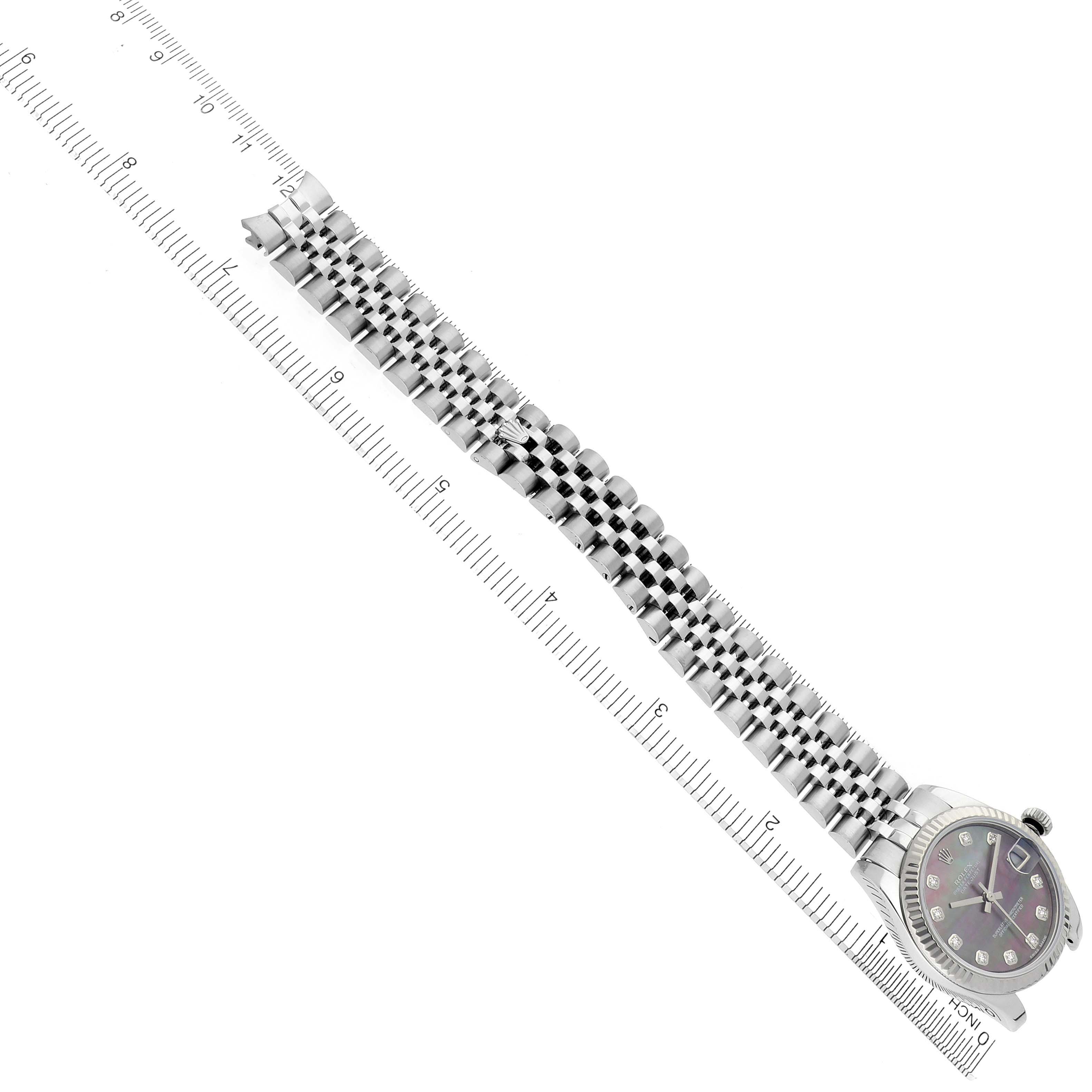 The Rolex Datejust watch is shown at an angled side view, displaying the face, bezel, and full bracelet laid flat beside a ruler.