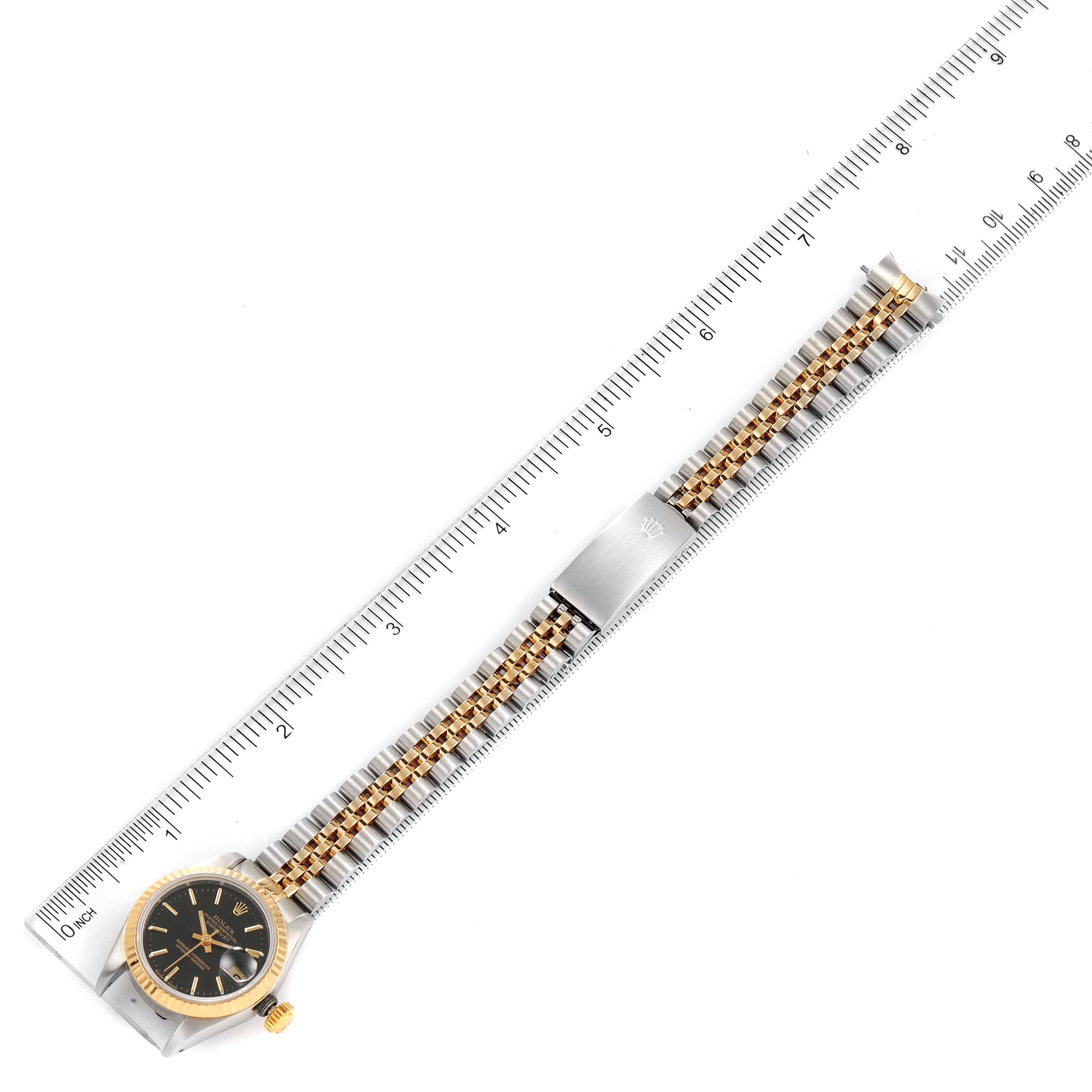 The image shows a flat-lay angle of a Rolex Datejust 69173 Women's Steel and Gold (two tone) Black Dial 69173 Women's Steel and Gold (two tone) Black Dial watch, highlighting its face, bezel, and two-tone jubilee bracelet alongside a ruler.