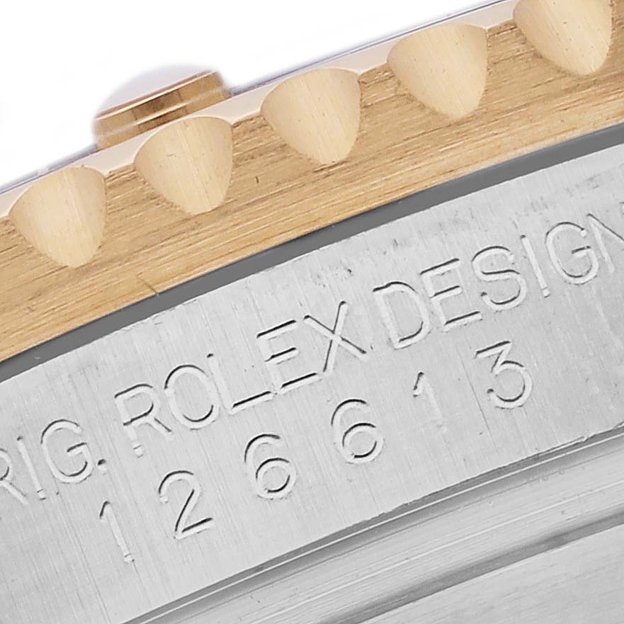 The image shows a close-up of the Rolex Submariner 126613LN Men's Steel and Gold (two tone) Black Dial 126613LN Men's Steel and Gold (two tone) Black Dial's bezel edge with "ROLEX DESIGN 126613" engraved on the side.