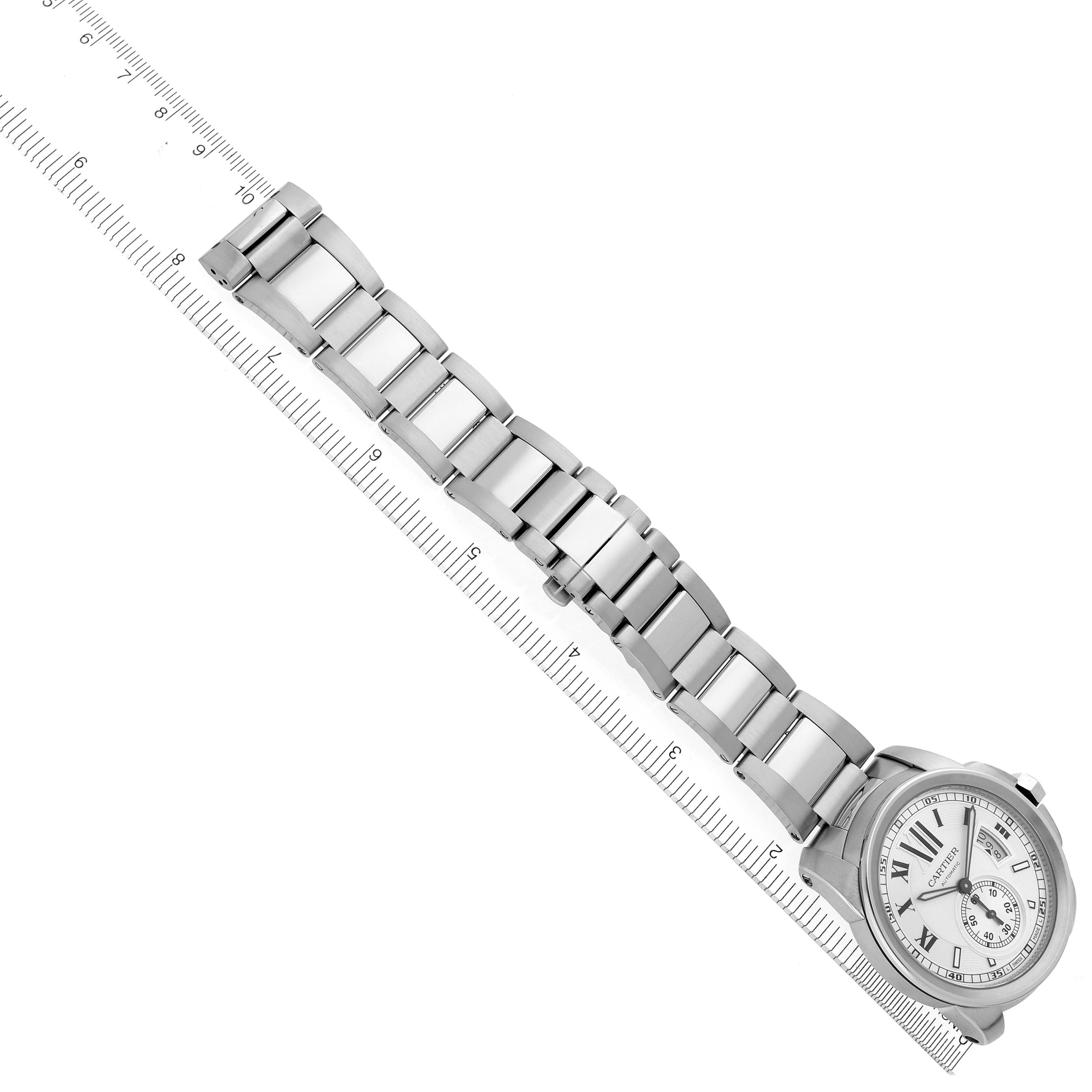 The image shows a Calibre de Cartier watch by Cartier from above, displaying the watch face and metal strap aligned with a ruler.