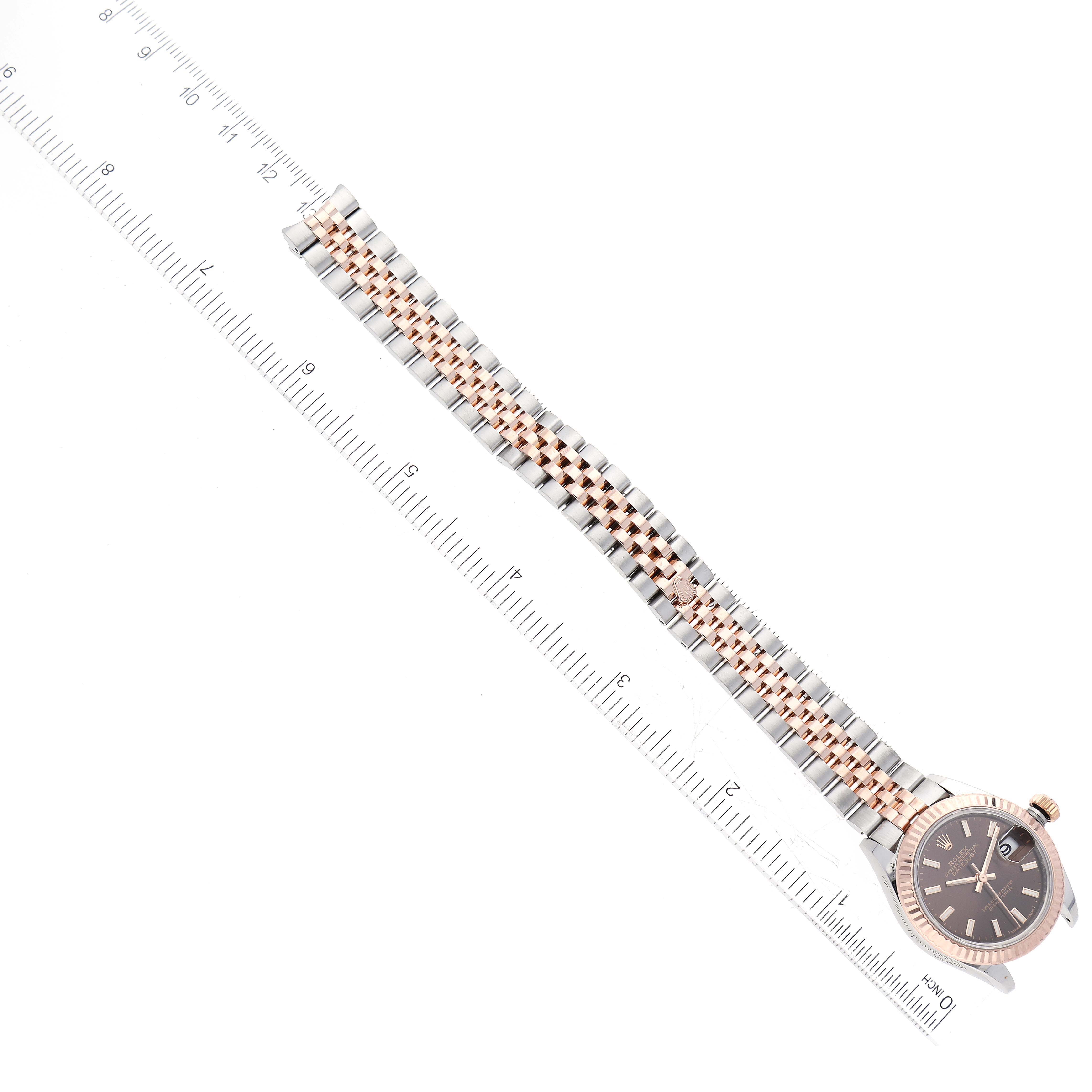 The image shows an aerial view of a Rolex Datejust 279171 Women's Steel and Gold (two tone) Brown Dial 279171 Women's Steel and Gold (two tone) Brown Dial watch, highlighting its metal strap and face against a ruler for scale.