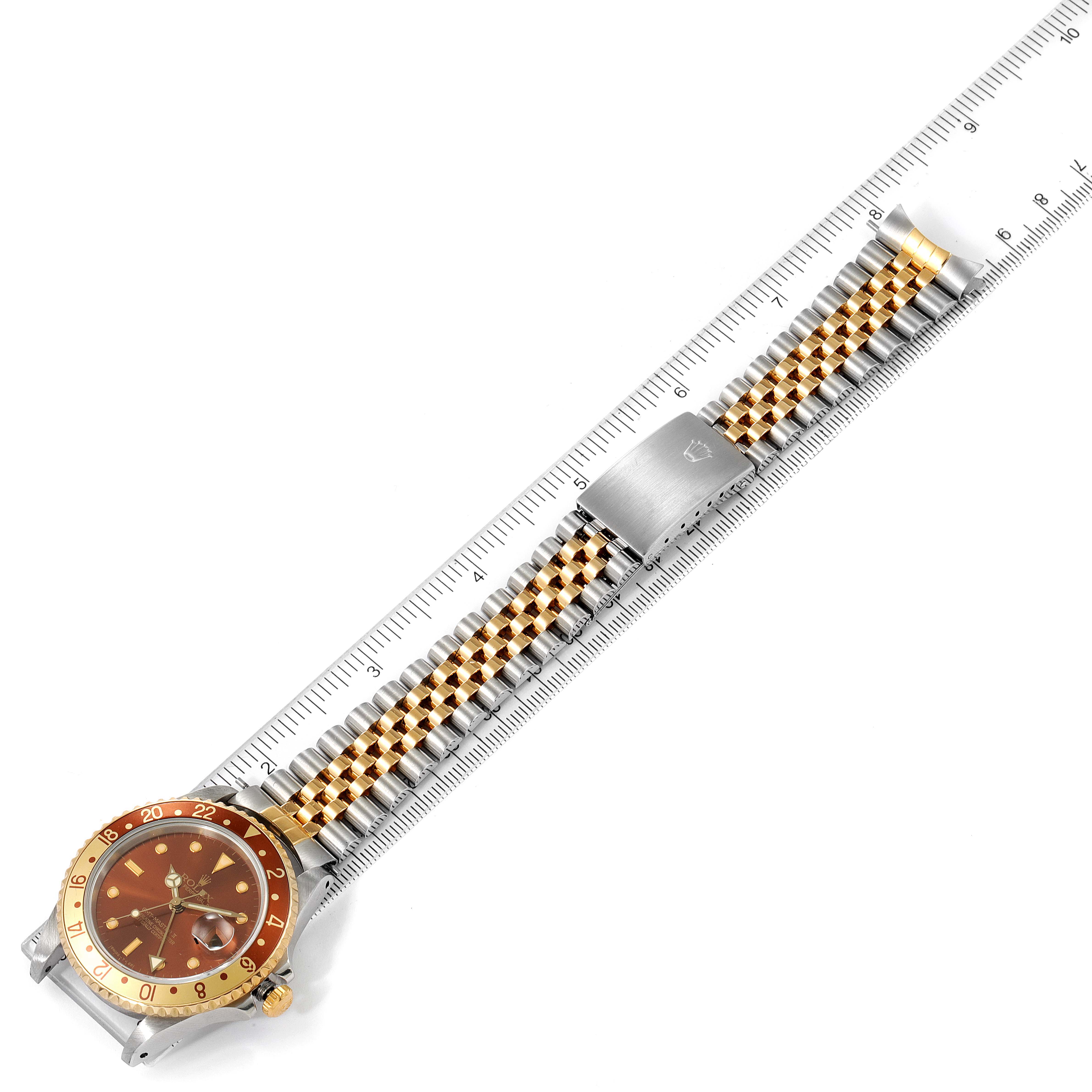 The image shows a top-down view of a Rolex GMT-Master 16713 Men's Steel and Gold (two tone) Brown Dial 16713 Men's Steel and Gold (two tone) Brown Dial watch with a gold and stainless steel bracelet next to a ruler for scale.