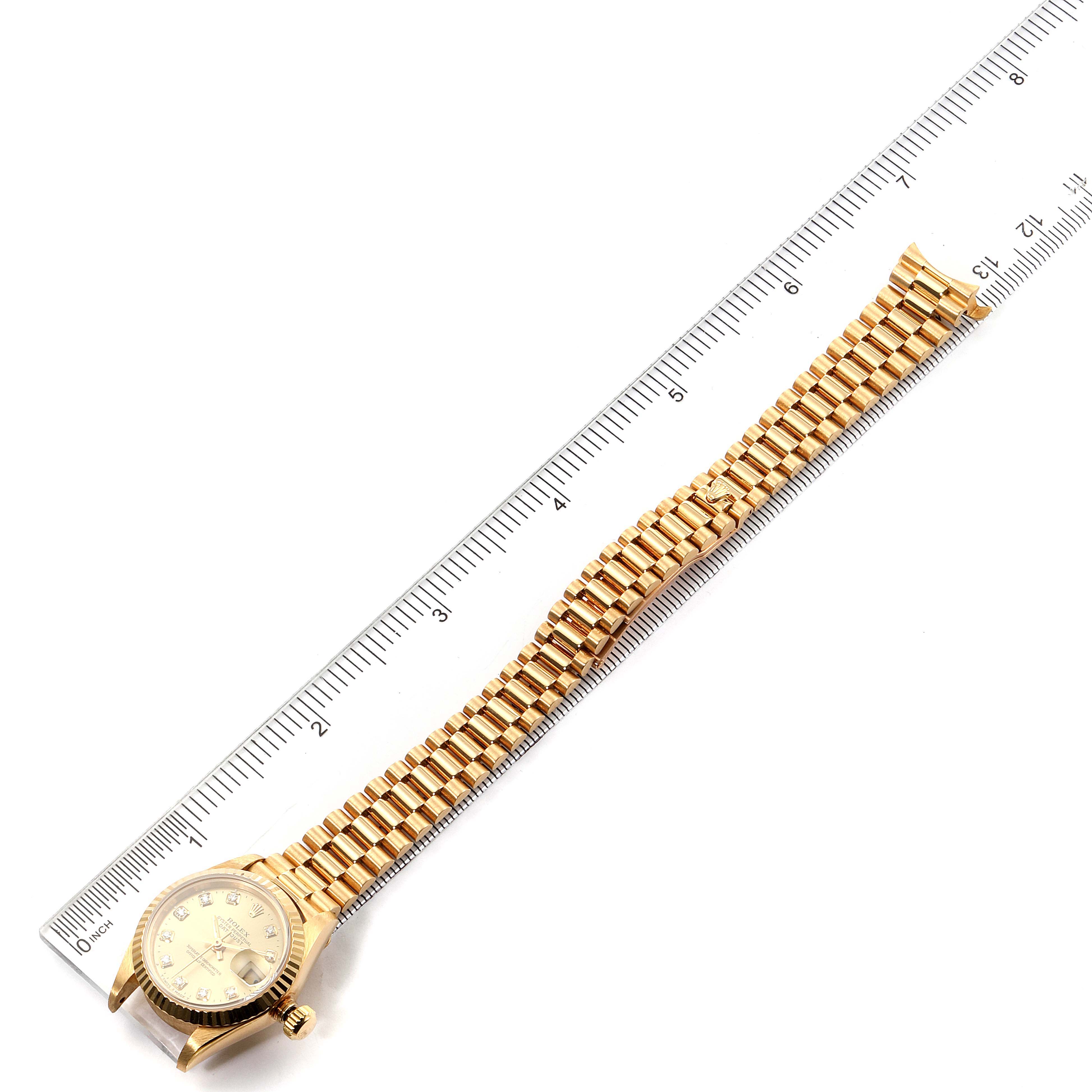 The image shows a Rolex President 69178 Women
s Yellow Gold Champagne Dial 69178 Women
s Yellow Gold Champagne Dial model watch laid flat against a ruler, displaying the entire gold bracelet and face.