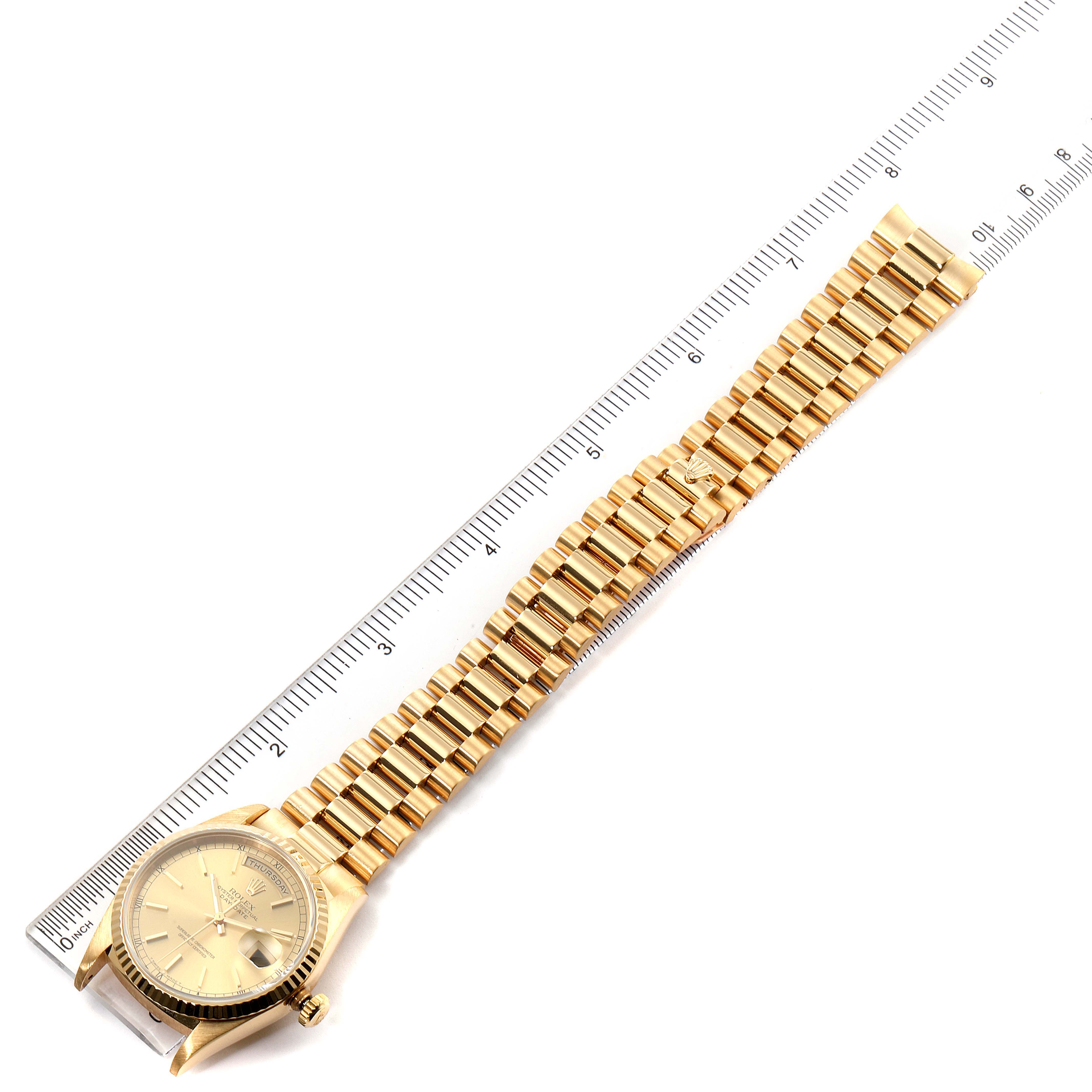 The Rolex President 18238 Men's Yellow Gold Champagne Dial 18238 Men's Yellow Gold Champagne Dial watch is shown flat with its face and gold bracelet aligned alongside a ruler.