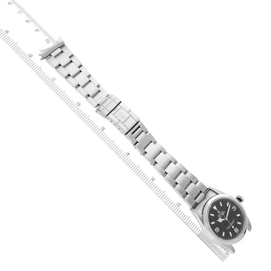 The Rolex Explorer 14270 Men's Stainless Steel Black Dial watch is shown at an angled top view, displaying the full bracelet and clasp alongside a ruler for scale.