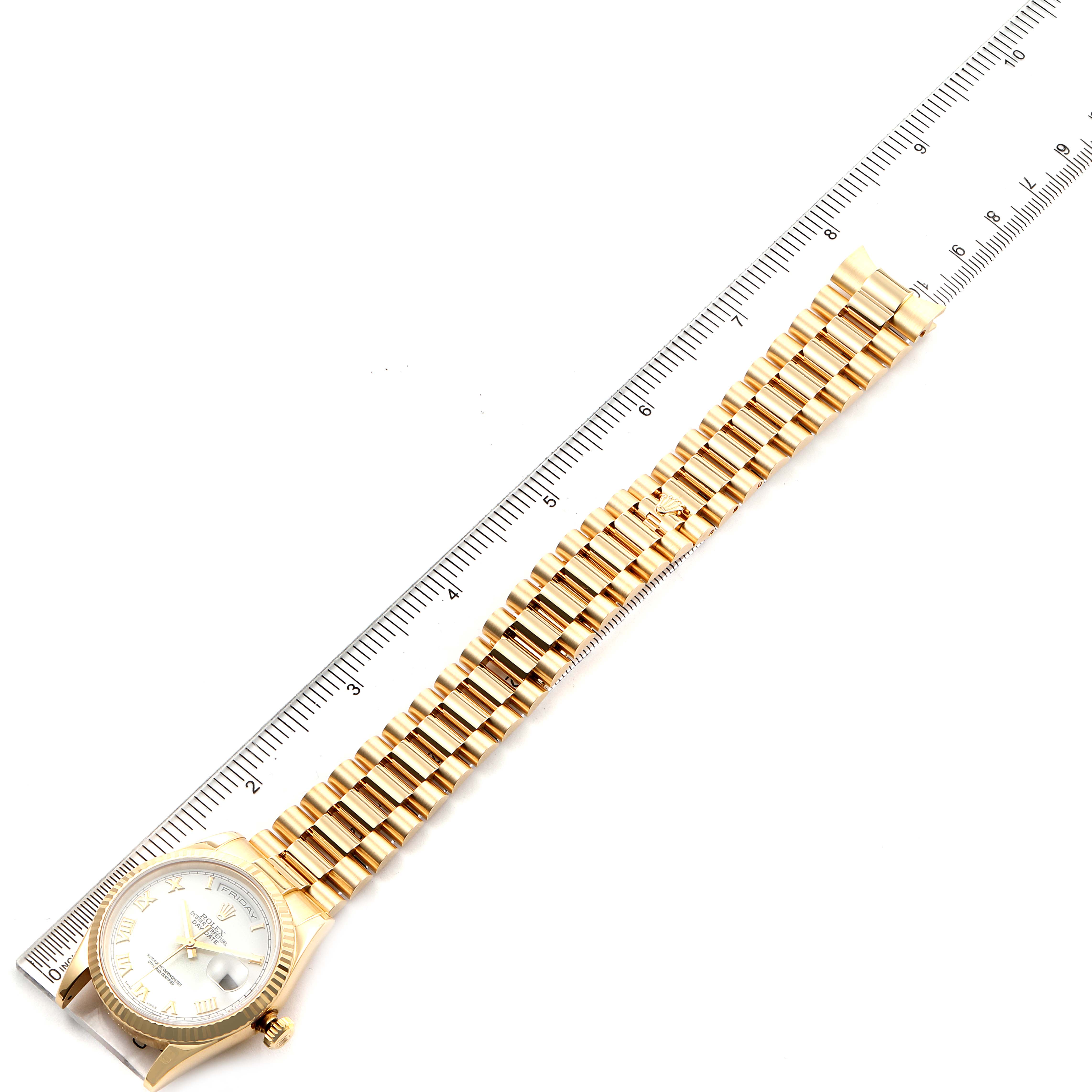 A Rolex President 118238 Men
s Yellow Gold White Dial 118238 Men
s Yellow Gold White Dial model watch is shown flat with its gold bracelet extended next to a ruler for measurement.