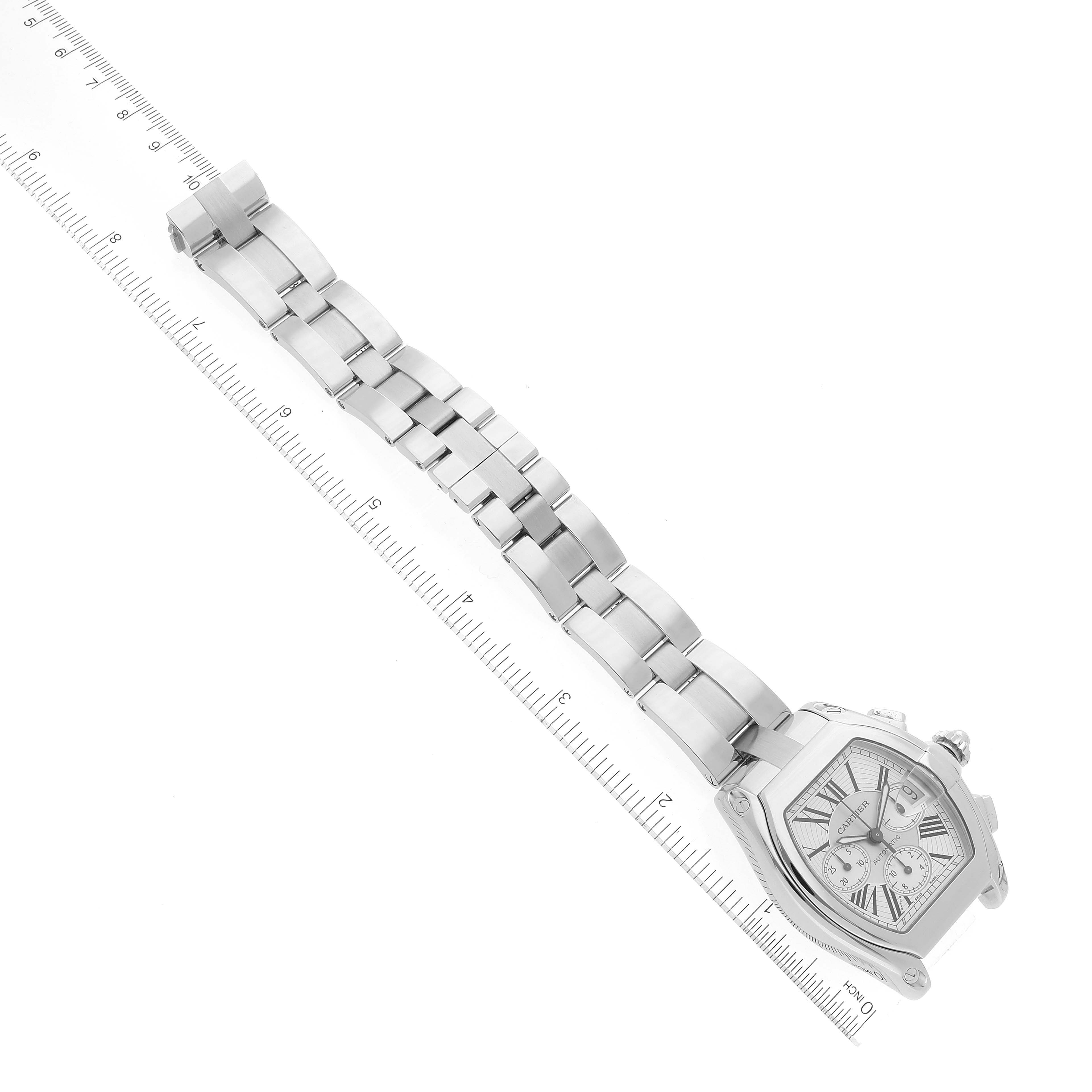 The image shows a Cartier Roadster W62019X6 Men's Stainless Steel Silver Dial W62019X6 Men's Stainless Steel Silver Dial watch laid flat next to a ruler, displaying its band and the face at an angle to the right.
