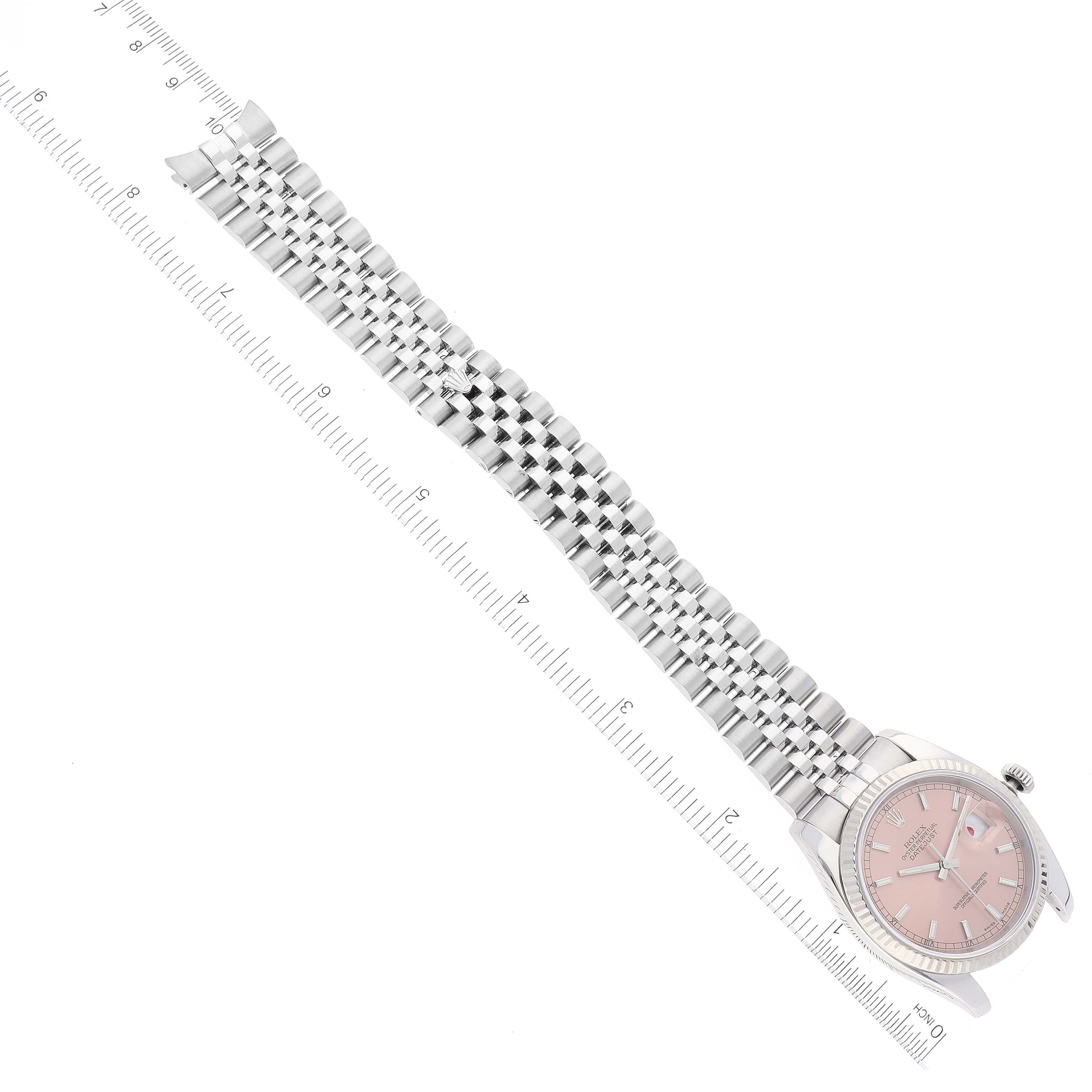 The image shows a top-down view of a Rolex Datejust 116234 Men's Stainless Steel Pink Dial 116234 Men's Stainless Steel Pink Dial watch with a pink dial and silver jubilee bracelet laid out flat with a ruler.