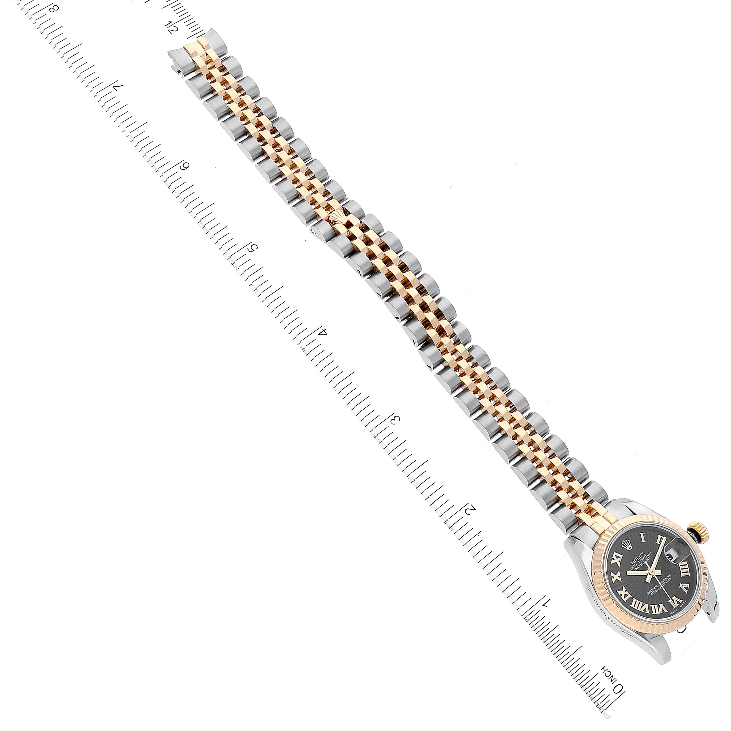 The image shows an overhead view of a Rolex Datejust 179173 Women's Steel and Gold (two tone) Black Dial 179173 Women's Steel and Gold (two tone) Black Dial watch, highlighting the dial, bezel, and two-toned bracelet next to a ruler.