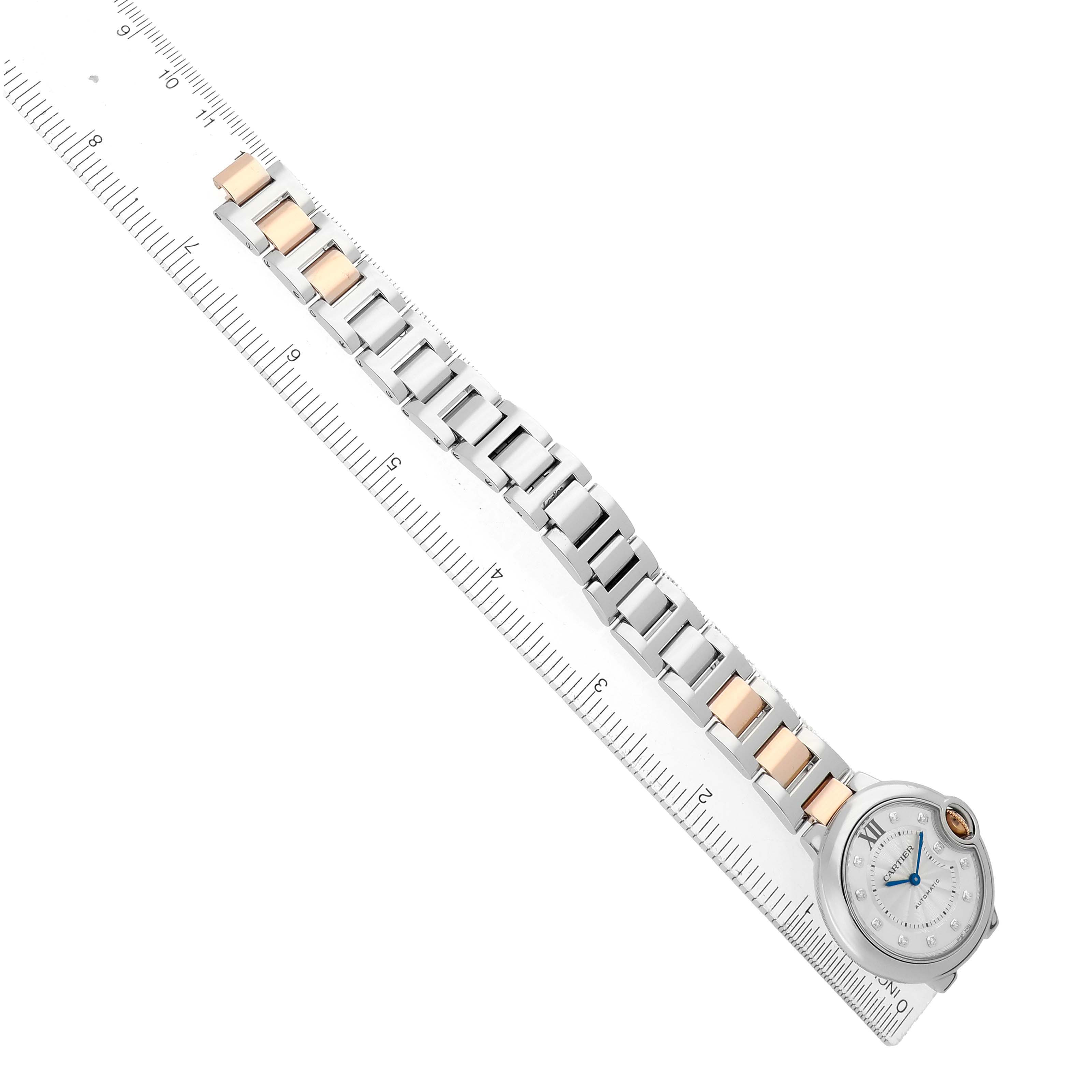 The Cartier Ballon Bleu WE902044 Women's Stainless Steel Silver Dial watch is shown from above, highlighting its face and metal bracelet on a ruler.