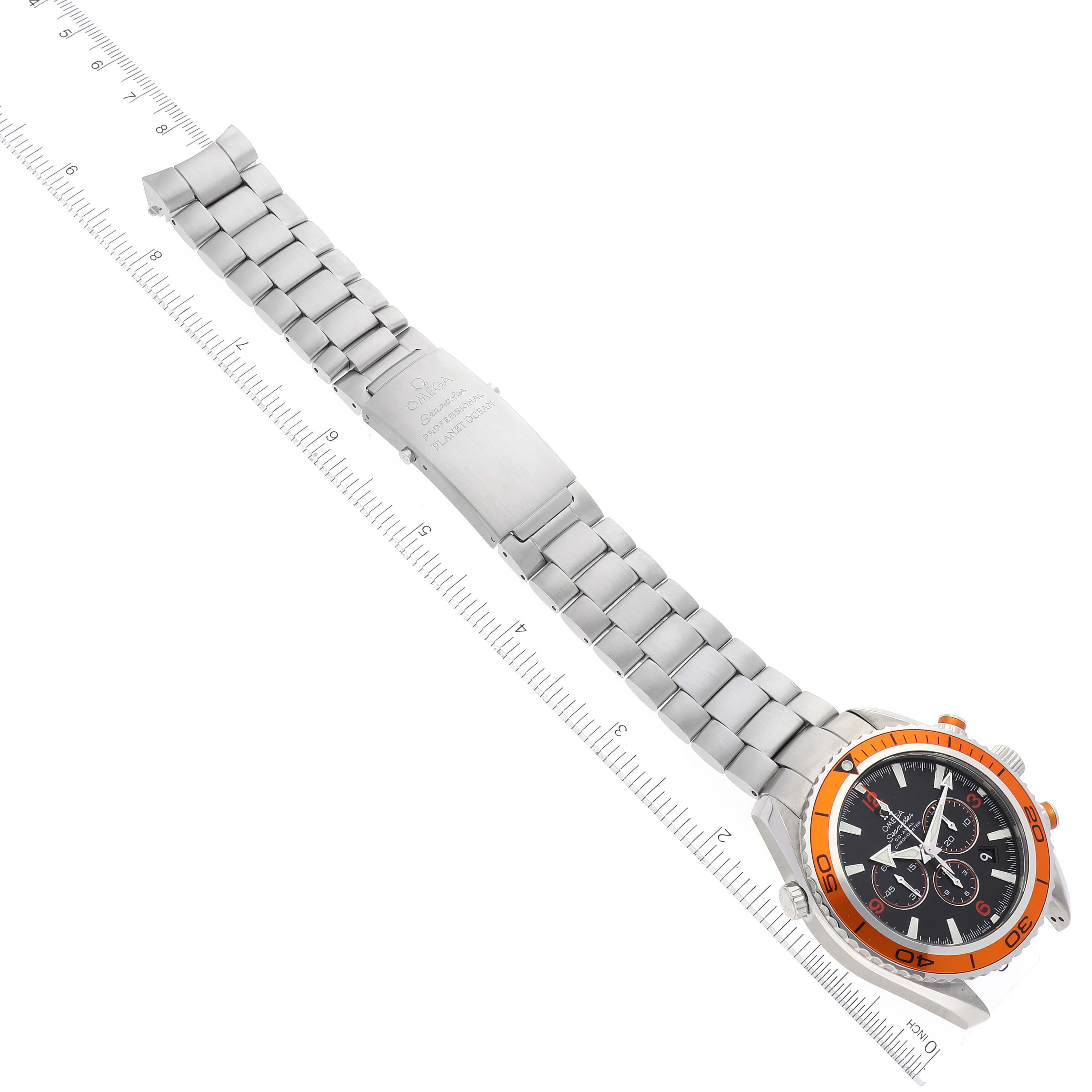 The image shows an Omega Planet Ocean 2218.50.00 Men
s Stainless Steel Black Dial 2218.50.00 Men
s Stainless Steel Black Dial watch at a diagonal angle, featuring its stainless steel bracelet, clasp, and dial with an orange bezel.