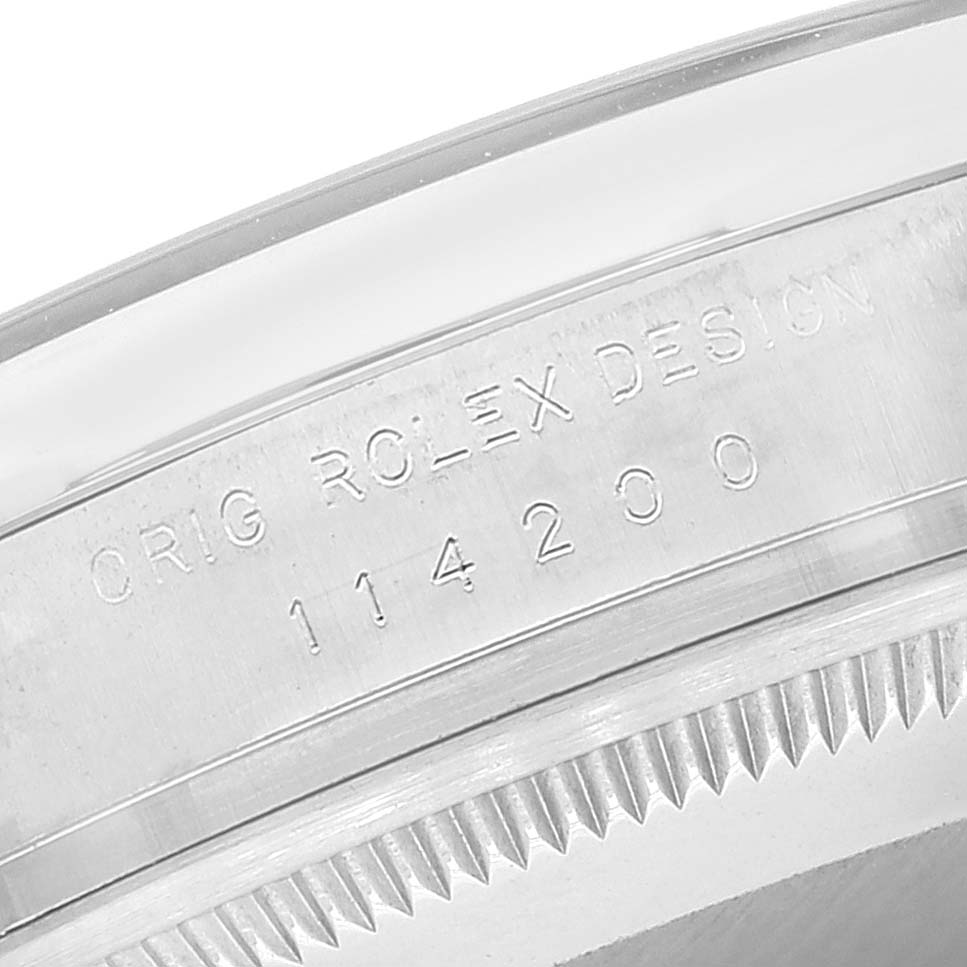 The image shows a close-up of the side and edge of a Rolex Air-King 114200 Men's Stainless Steel Silver Dial 114200 Men's Stainless Steel Silver Dial watch, highlighting its engraving and part of the bezel.