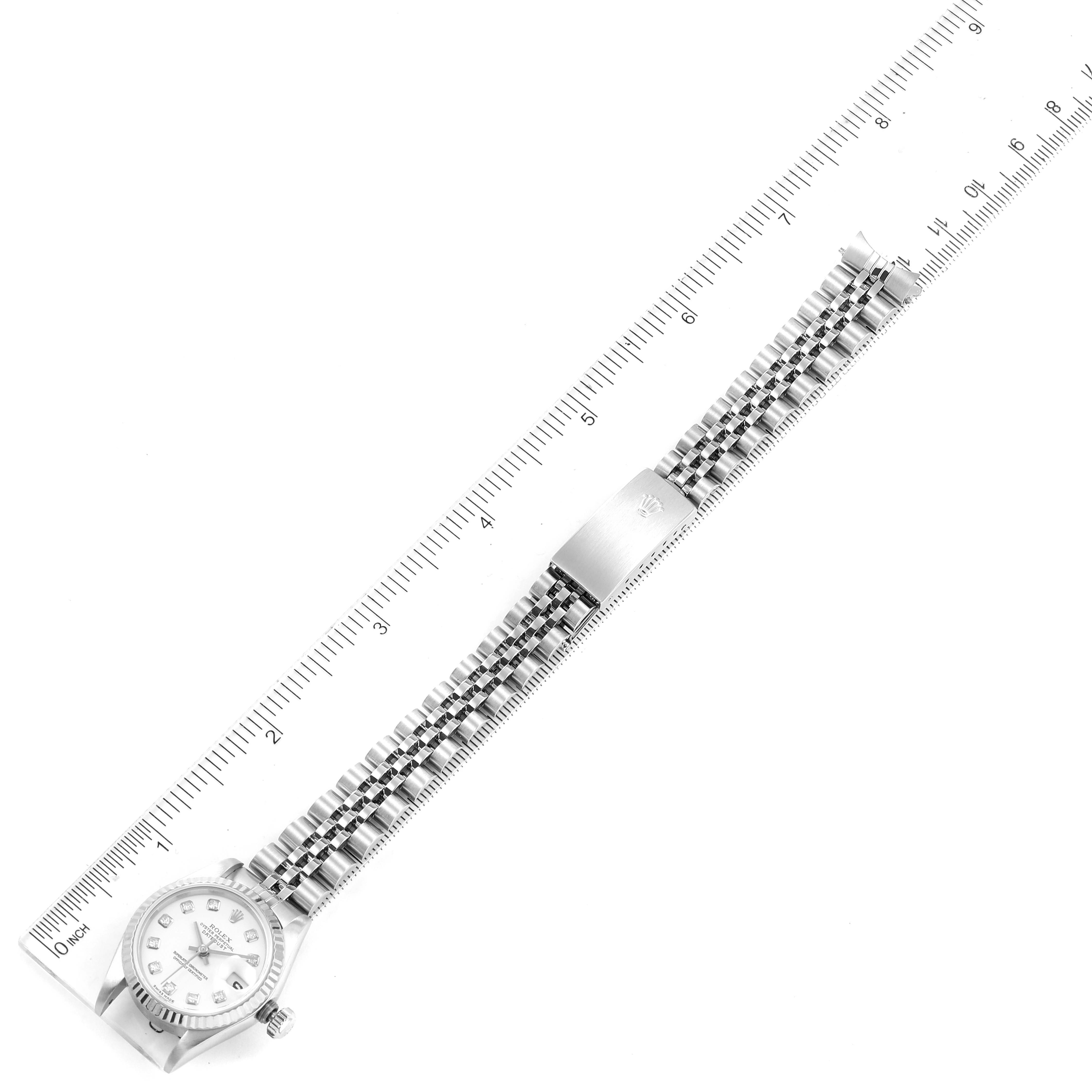 This top-down image shows the Rolex Datejust 79174 Women's Stainless Steel White Dial 79174 Women's Stainless Steel White Dial watch face, bezel, crown, and bracelet fully extended alongside a ruler.