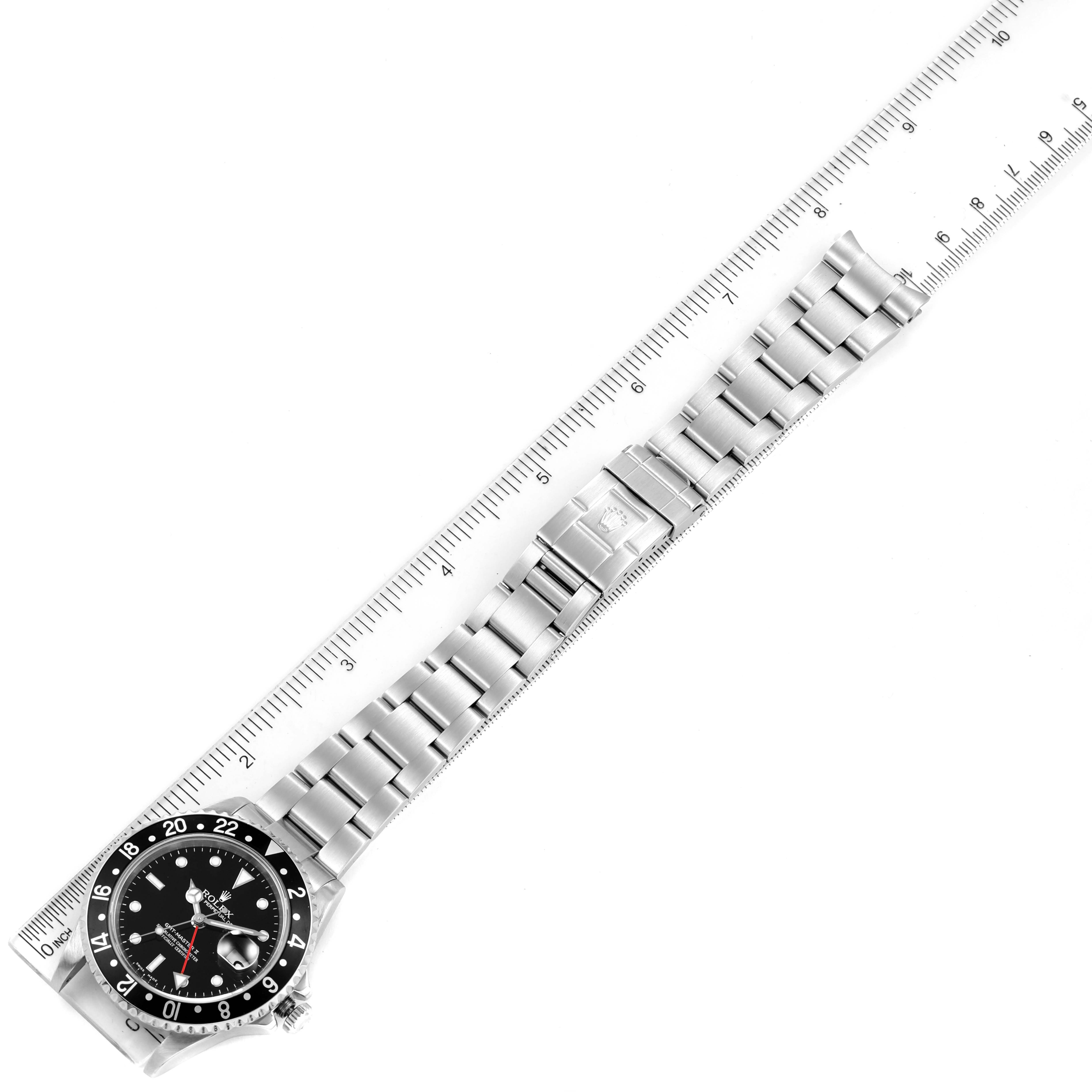 This image shows a top-down view of a Rolex GMT-Master 16710 Men
s Stainless Steel Black Dial 16710 Men
s Stainless Steel Black Dial watch, displaying its face and stainless steel bracelet next to a ruler.