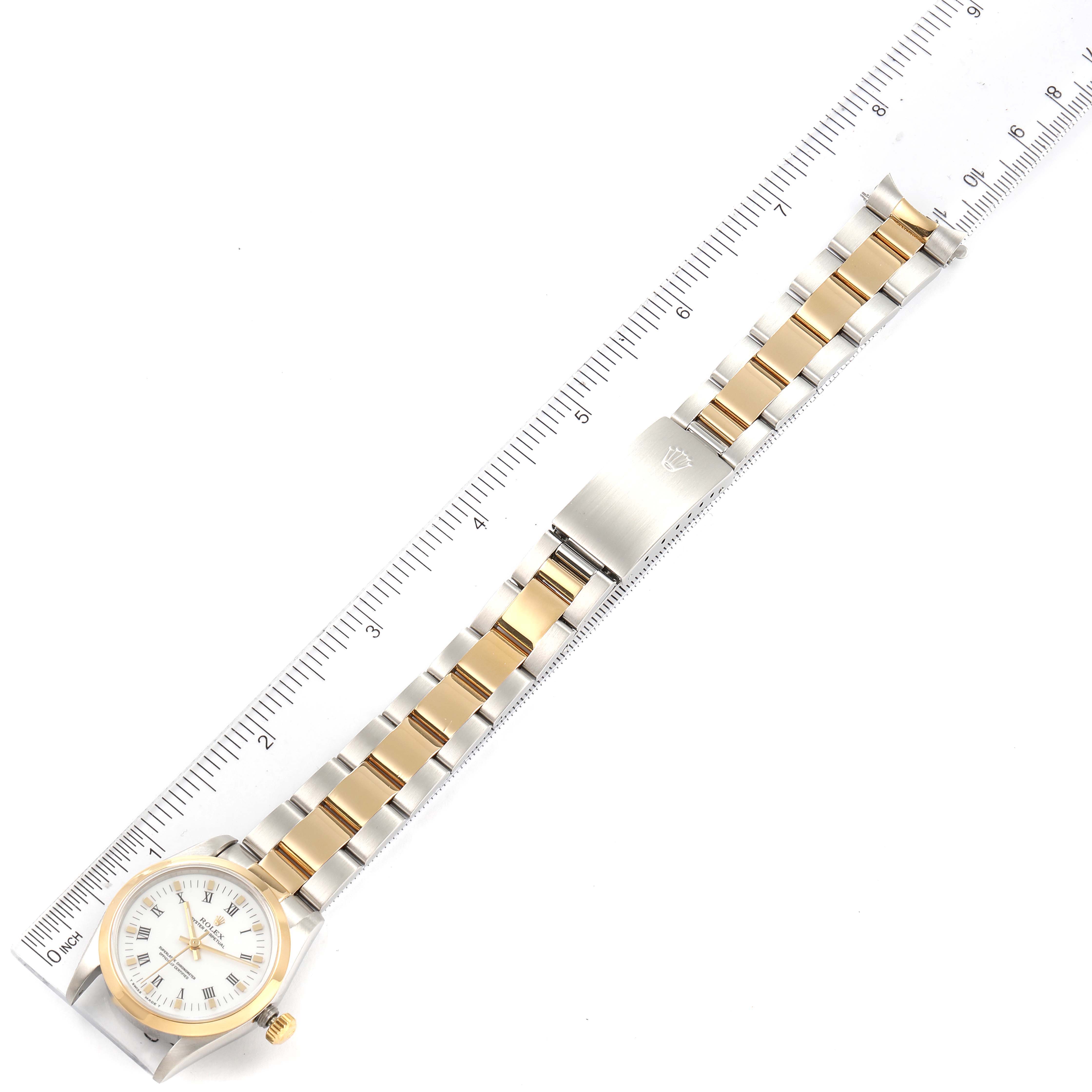 The image shows a top-down view of a mid-size Rolex watch, displaying the face, bezel, and two-tone bracelet next to a ruler.