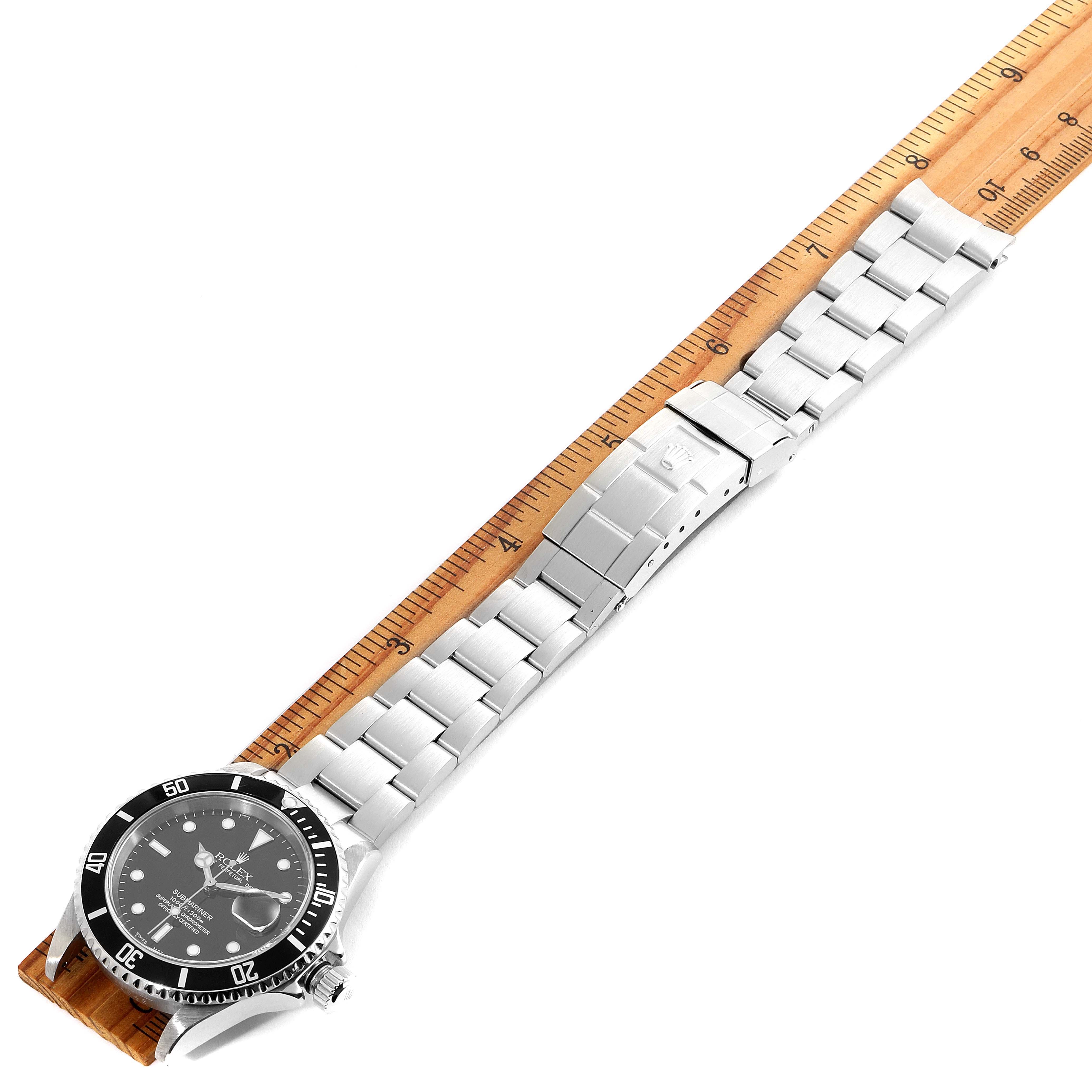 This image shows a Rolex Submariner 16610 Men
s Stainless Steel Black Dial 16610 Men
s Stainless Steel Black Dial watch laid flat next to a ruler, displaying its face, bezel, case, and entire bracelet.