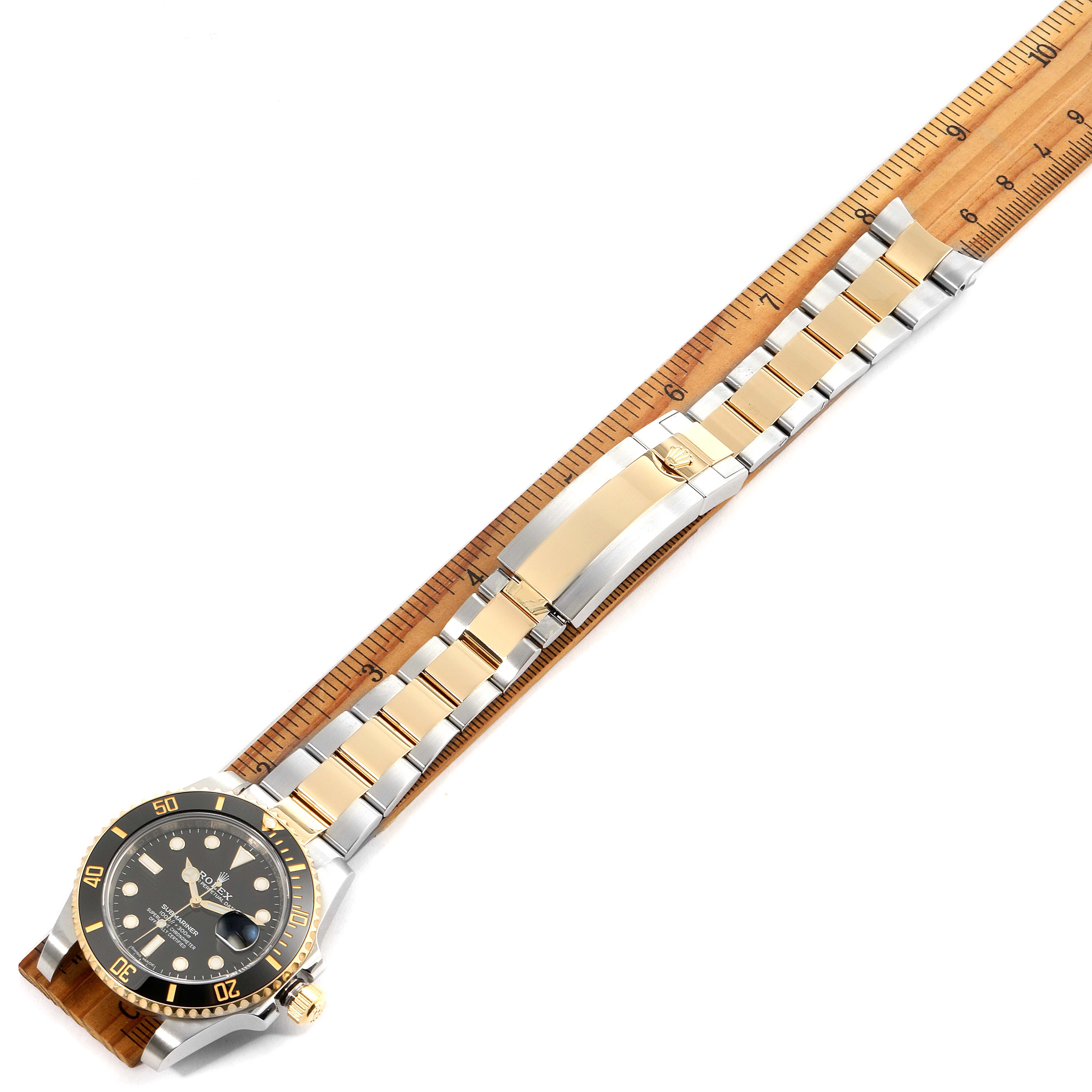 This image shows a Rolex Submariner 116613 Men's Steel and Gold (two tone) Black Dial 116613 Men's Steel and Gold (two tone) Black Dial model watch laid flat next to a ruler, displaying the watch face and metal bracelet.