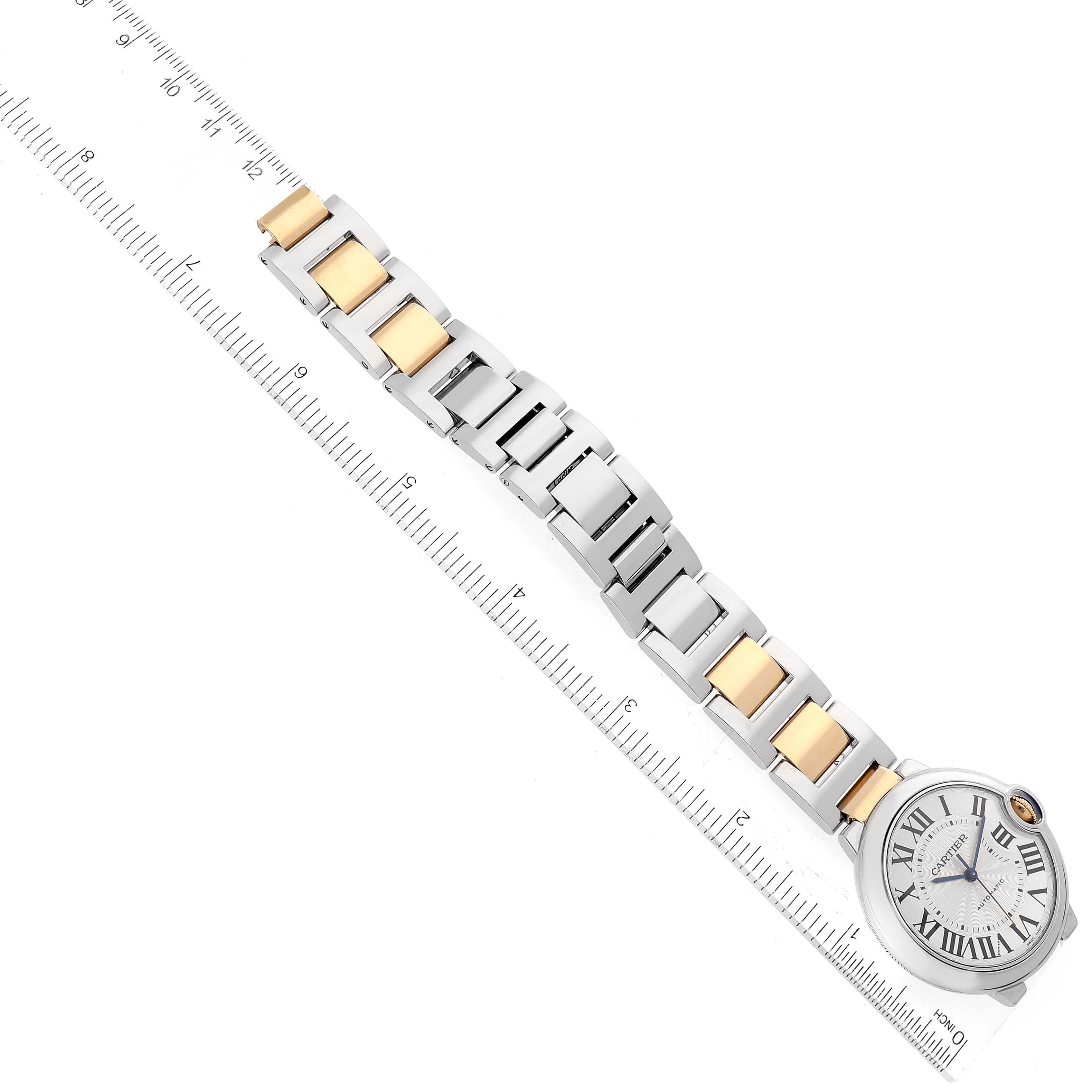 The image shows an overhead view of the Ballon Bleu de Cartier watch, featuring its face and metal bracelet next to a ruler.