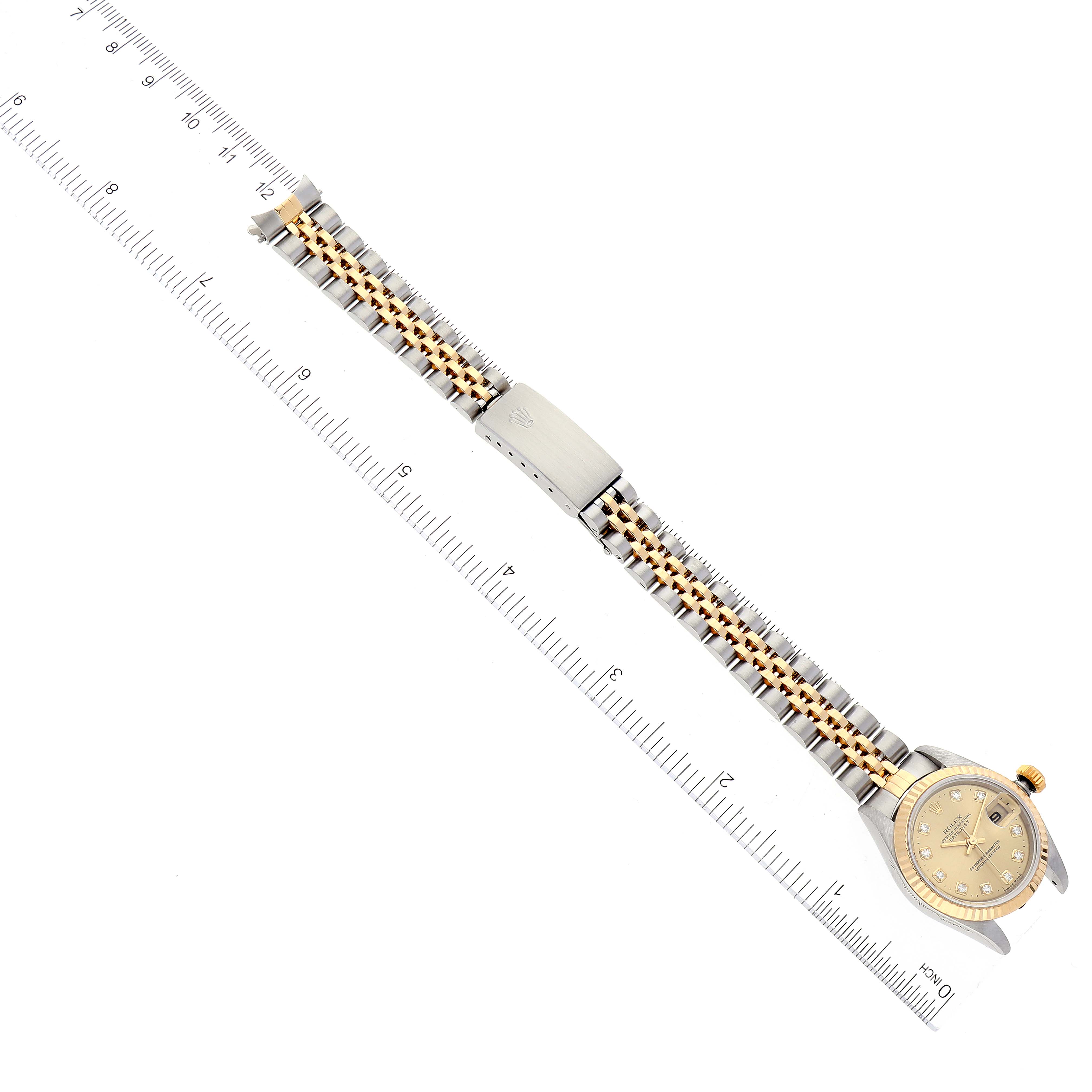 This image shows a Rolex Datejust 79173 Women's Steel and Gold (two tone) Champagne Dial 79173 Women's Steel and Gold (two tone) Champagne Dial watch laid flat alongside a ruler, displaying the entire bracelet and face.