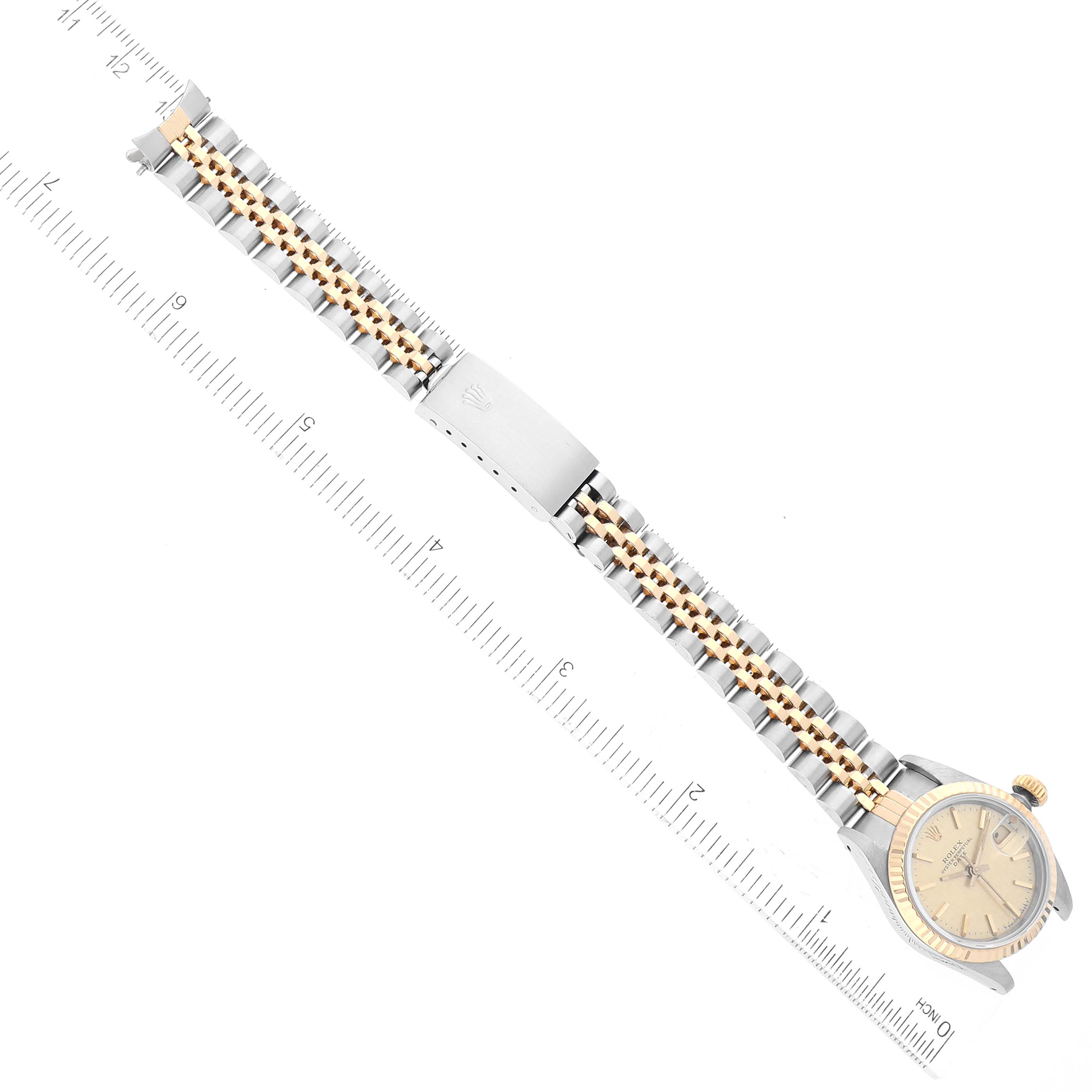 The Rolex Date 69173 Women's Steel and Gold (two tone) Champagne Dial 69173 Women's Steel and Gold (two tone) Champagne Dial watch is shown laid flat with its face, bezel, bracelet, and clasp visible, positioned alongside a ruler.
