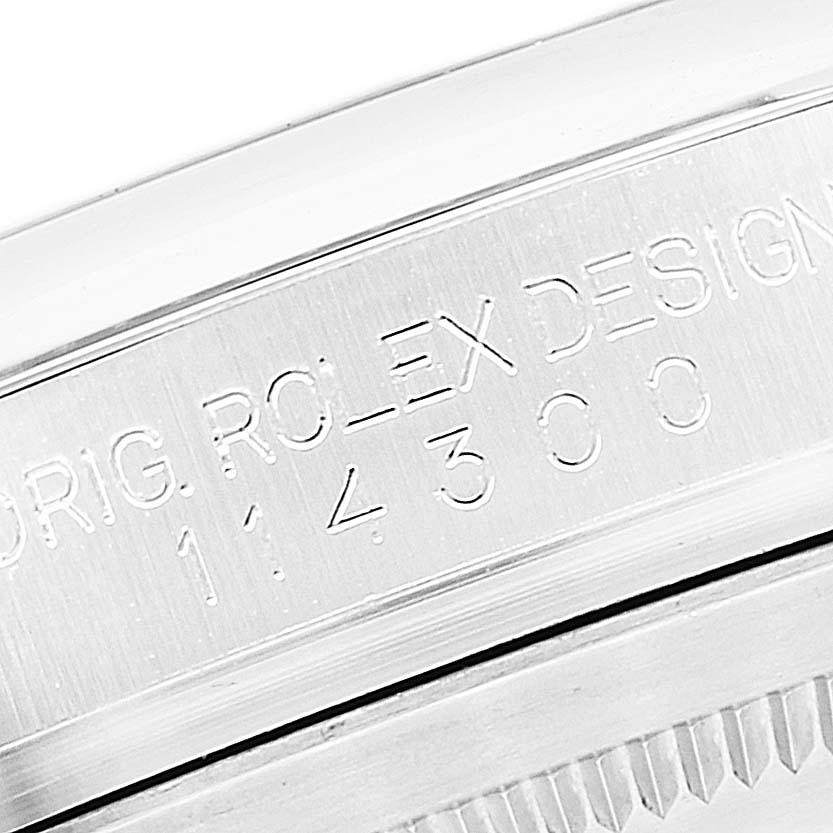 The image shows a close-up of the side of the watch case of the Rolex Oyster Perpetual 114300 Men's Stainless Steel Black Dial 114300 Men's Stainless Steel Black Dial, showing engraved markings.