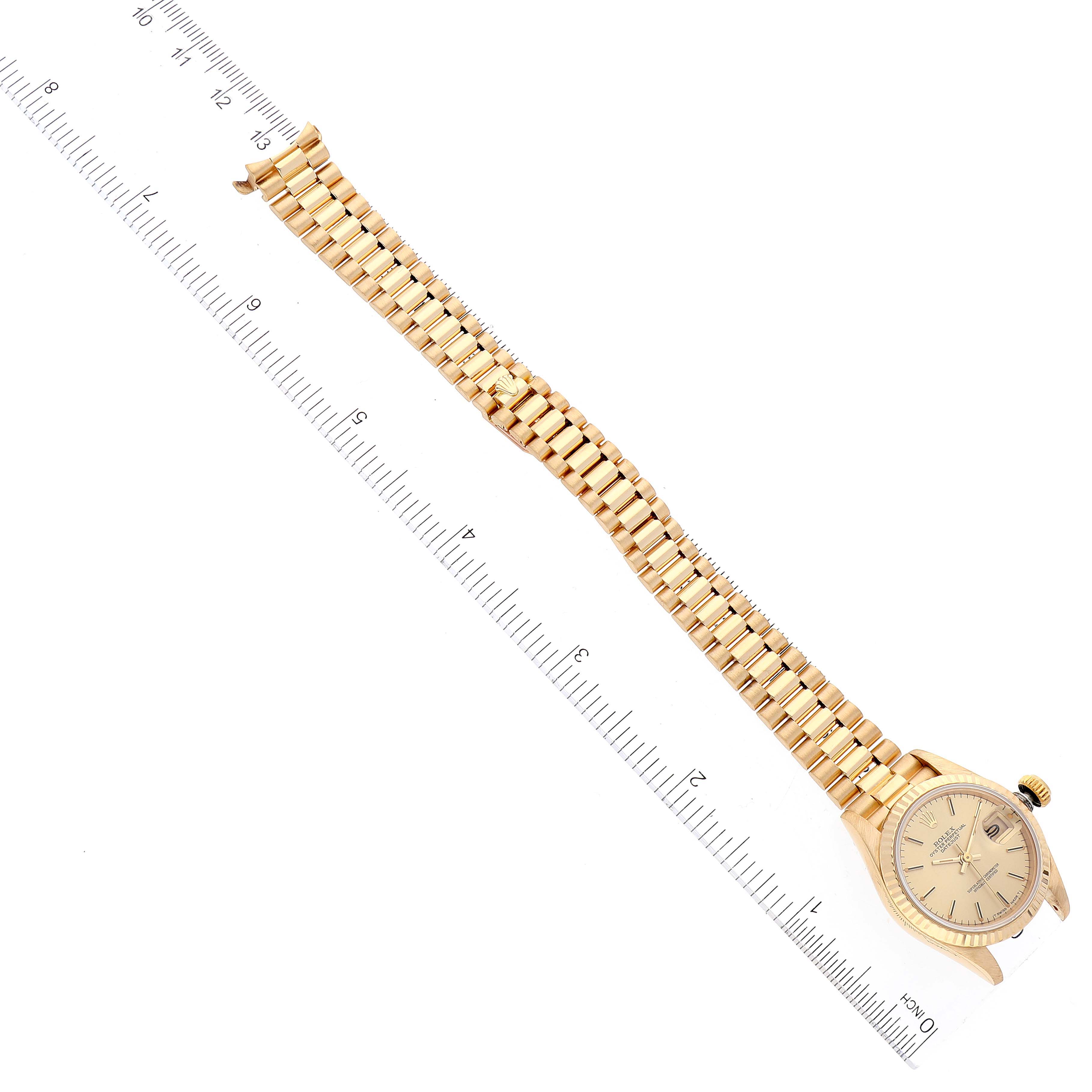 The image shows a Rolex President 69178 Women
s Yellow Gold Champagne Dial 69178 Women
s Yellow Gold Champagne Dial model watch laid flat, highlighting its gold bracelet and dial on a measuring scale.