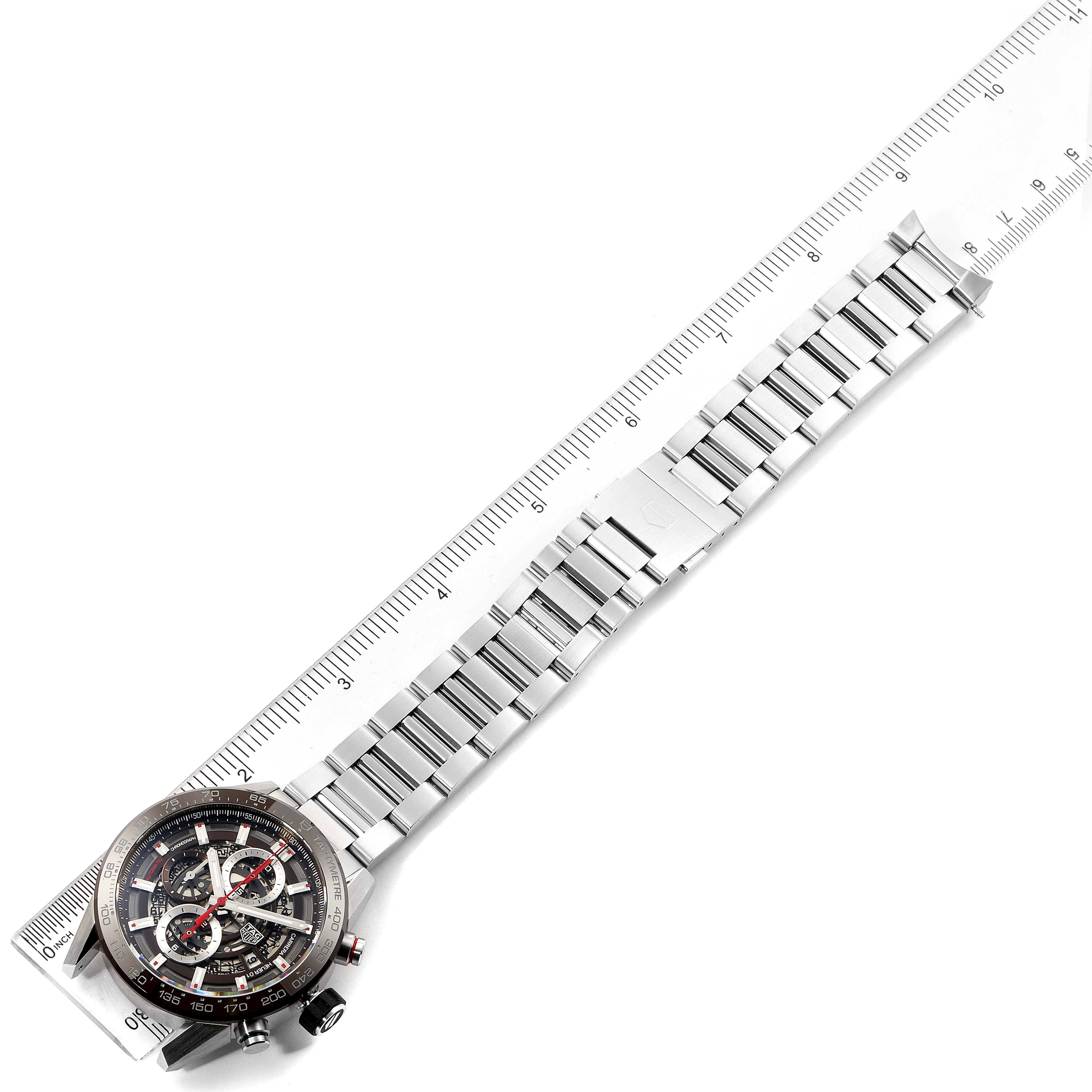 The image shows a full view of a Tag Heuer Carrera CAR201U.BA0766 Men's Stainless Steel Brown Dial CAR201U.BA0766 Men's Stainless Steel Brown Dial watch laid flat alongside a ruler, highlighting the watch face and metal bracelet.