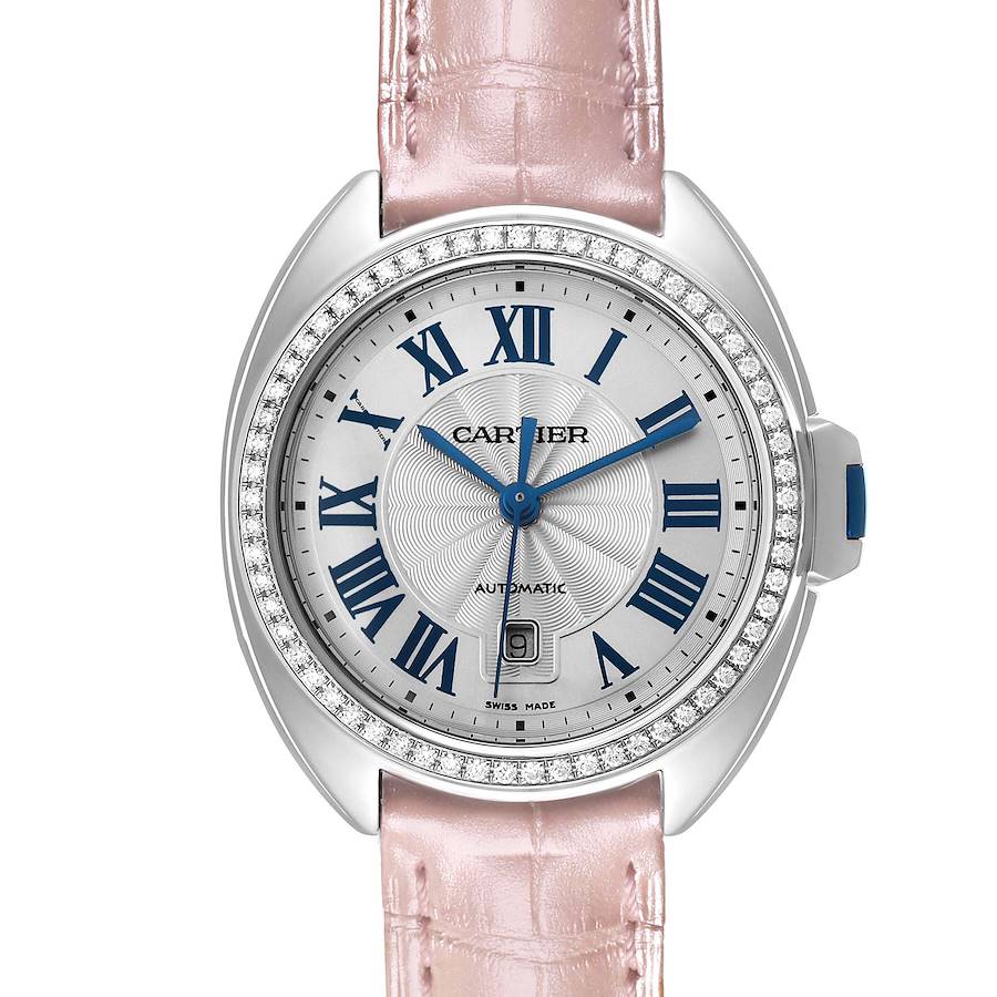 The Cartier Clé watch is shown from a front angle, displaying the dial, blue hands, Roman numerals, and pink strap.