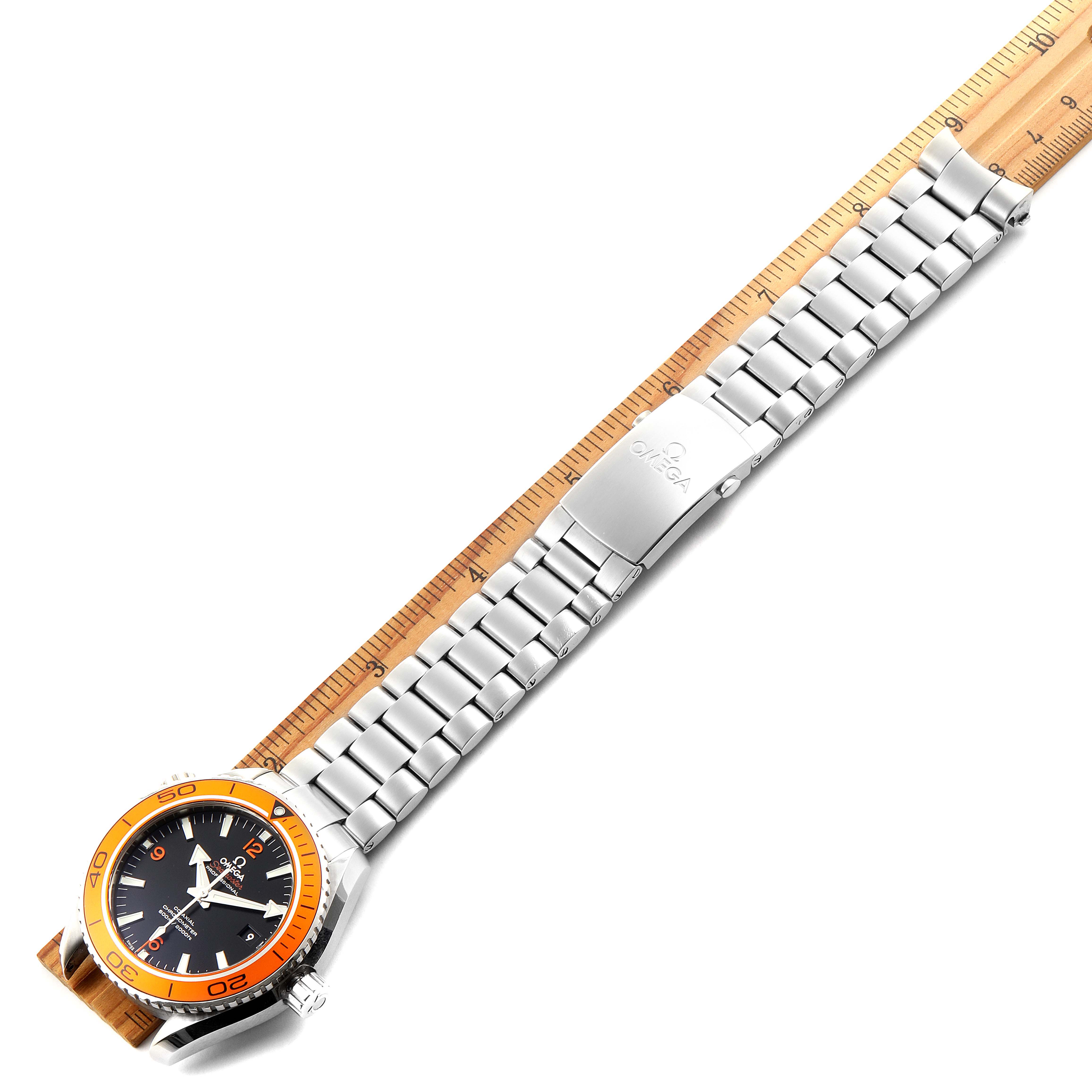 The Omega Planet Ocean 232.30.42.21.01.002 Men
s Stainless Steel Black Dial 232.30.42.21.01.002 Men
s Stainless Steel Black Dial watch is shown from a top-down angle, displaying the face, bezel, strap, and clasp on a ruler.