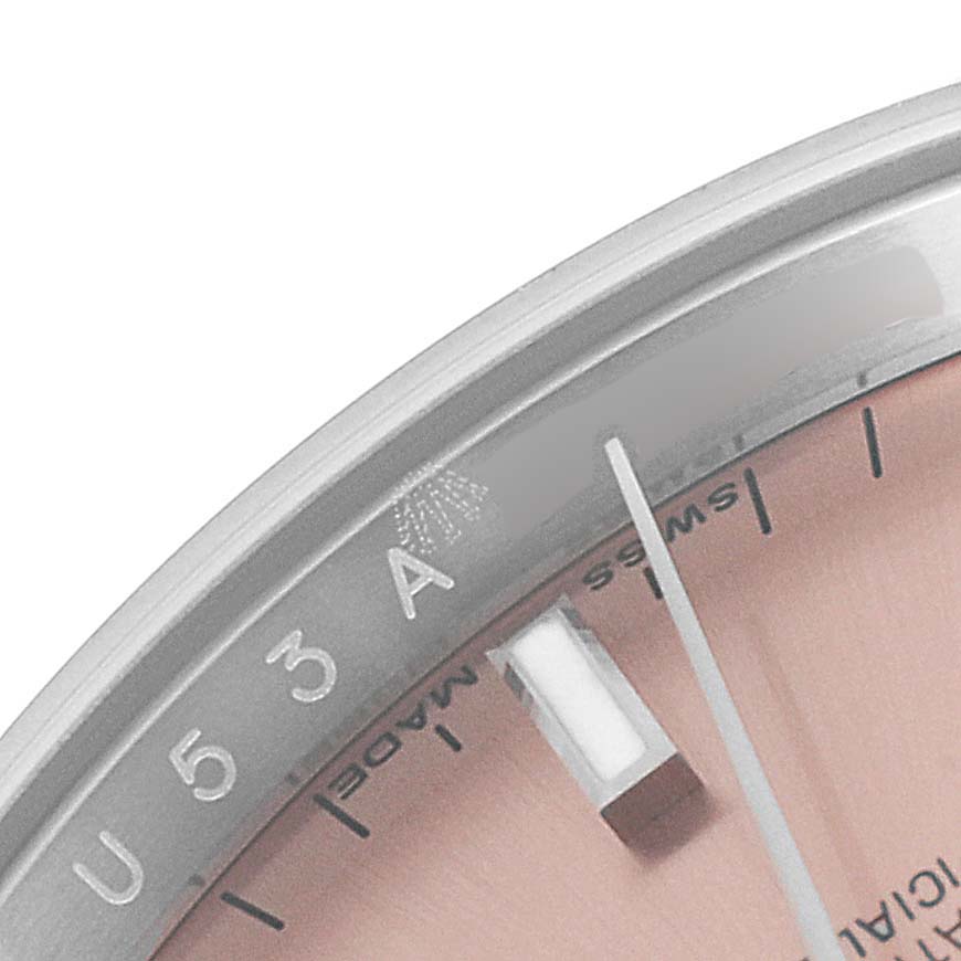 The image shows a close-up of the dial and edge of a Rolex Date 115200 Men's Stainless Steel Pink Dial 115200 Men's Stainless Steel Pink Dial model watch, displaying some hour markers and part of the logo.