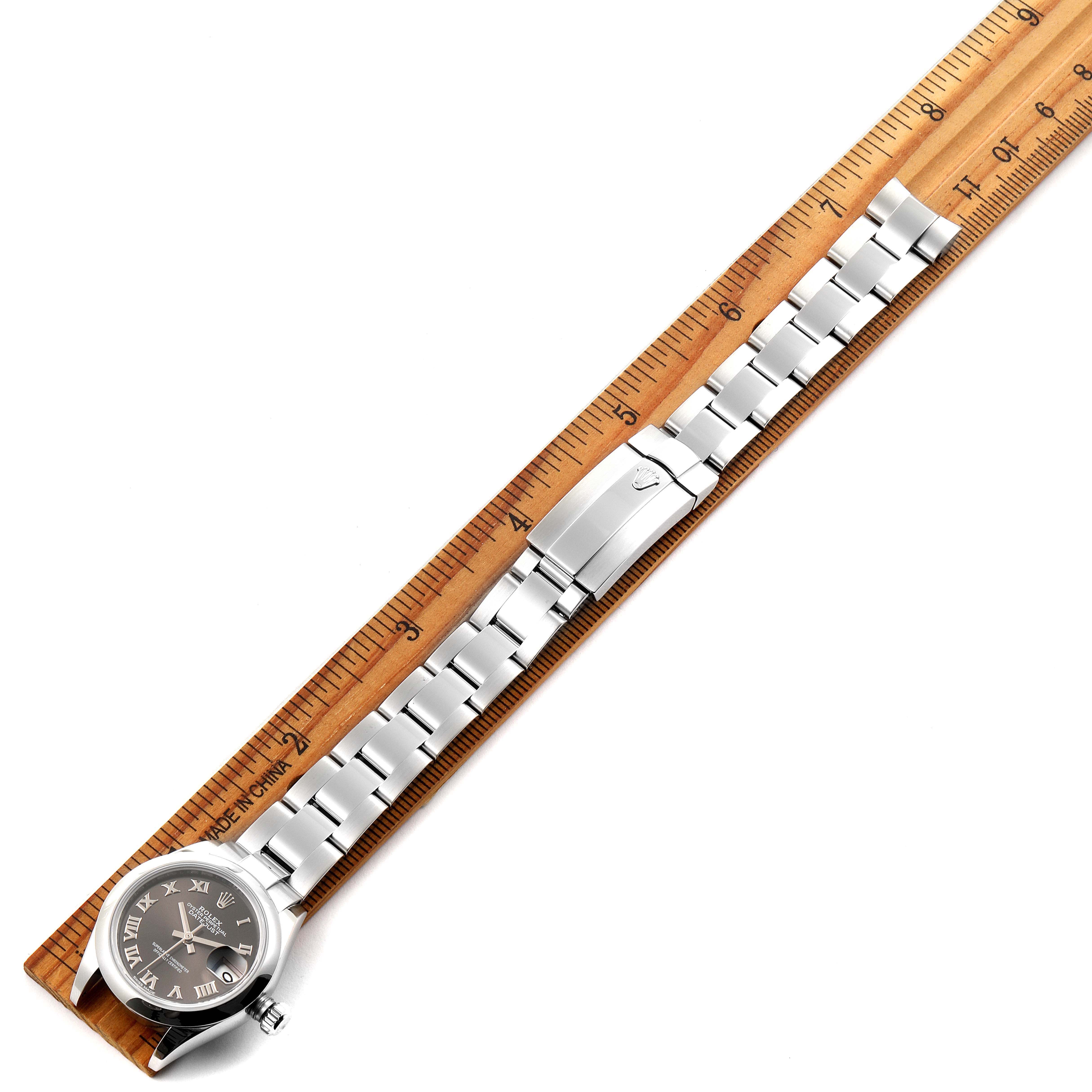 The Rolex Datejust 279160 Women's Stainless Steel Brown Dial 279160 Women's Stainless Steel Brown Dial watch is shown from a top-down angle, displaying the face, bracelet, and clasp, next to a ruler for measurement.
