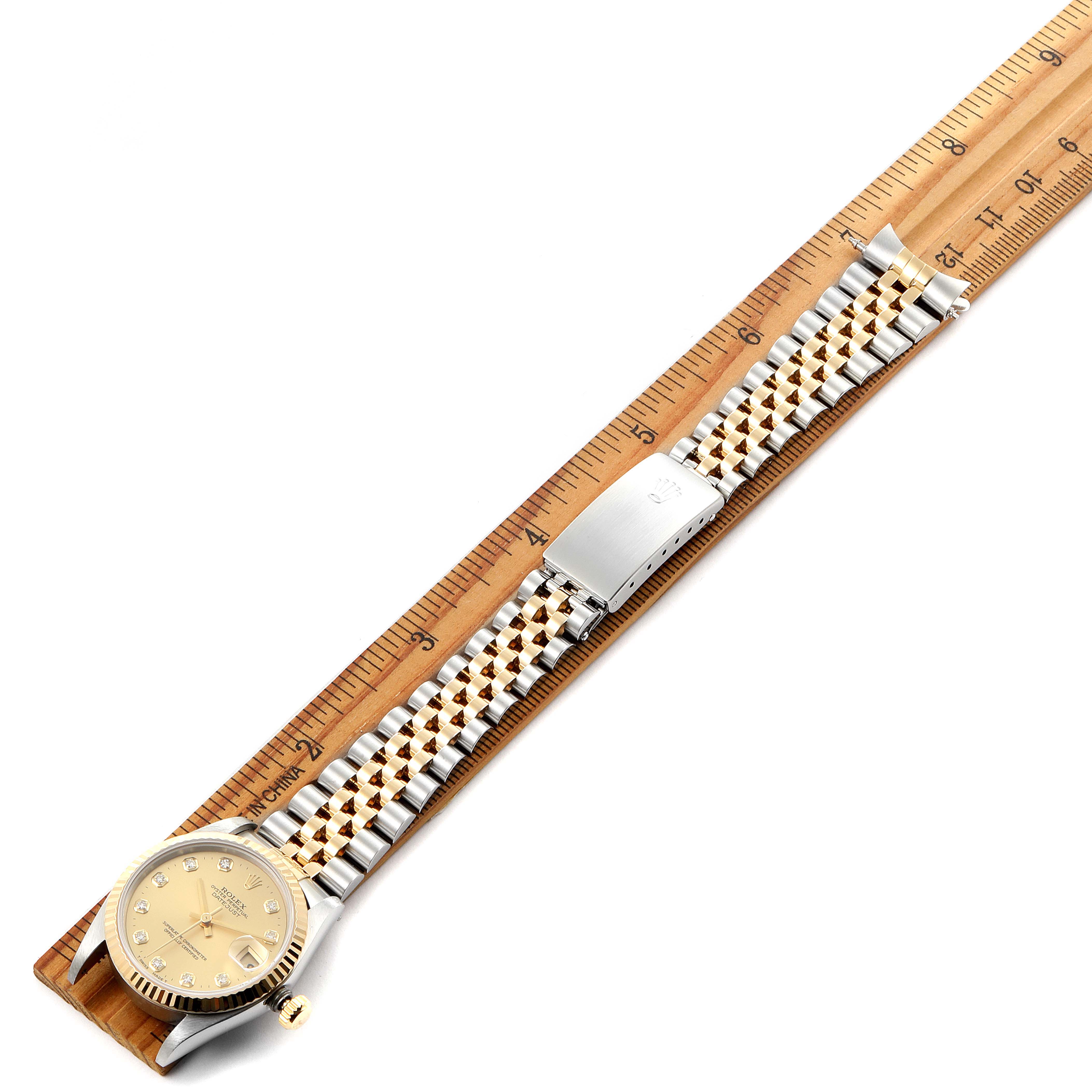 The Rolex Mid-Size 68273 Women's Stainless Steel Champagne Dial 68273 Women's Stainless Steel Champagne Dial watch is shown laid flat at an angle, with both the face and band visible, alongside a ruler for scale.