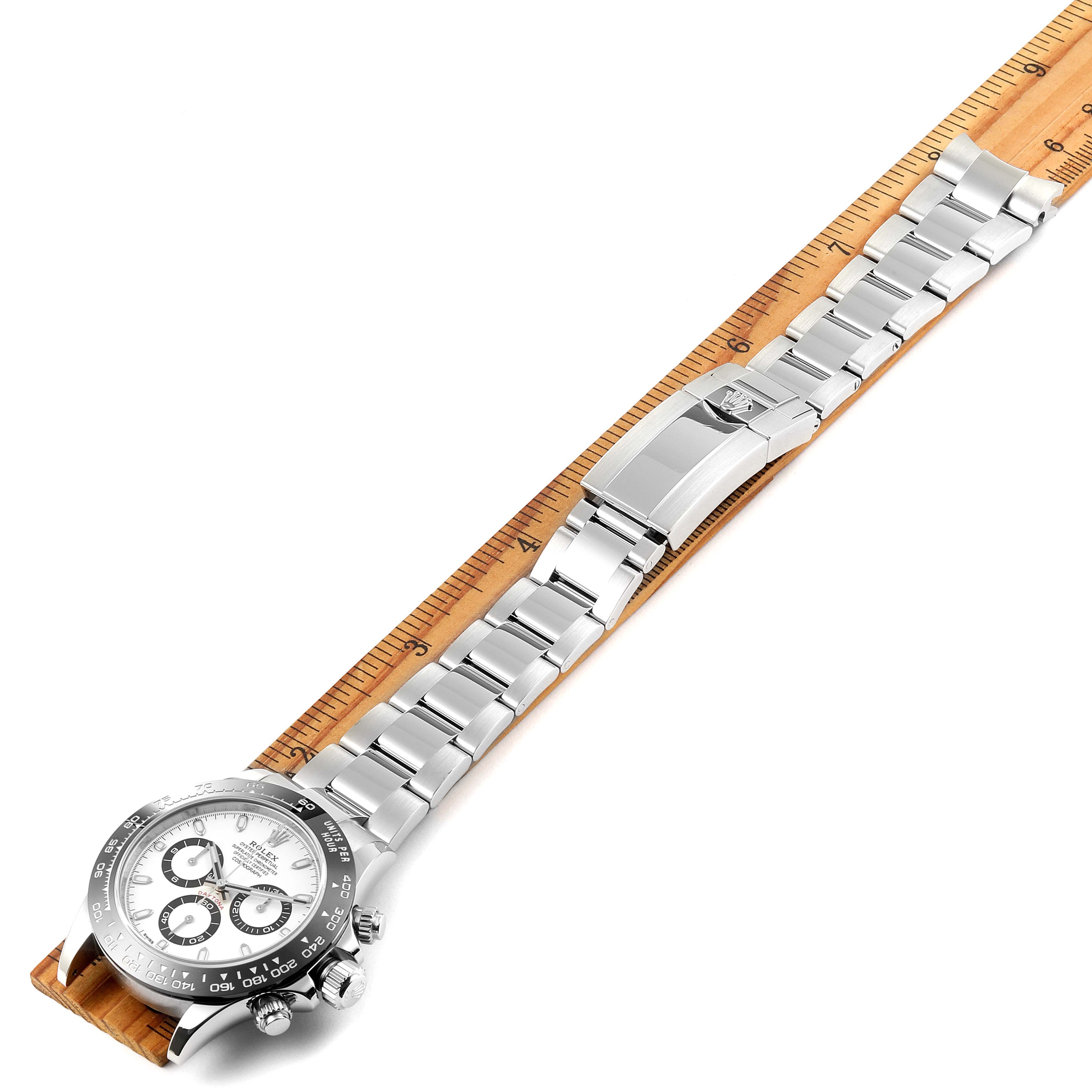 The image shows the Rolex Daytona 116500 Men's Stainless Steel White Dial 116500 Men's Stainless Steel White Dial watch face, crown, chronograph buttons, and bracelet against a ruler for size comparison.