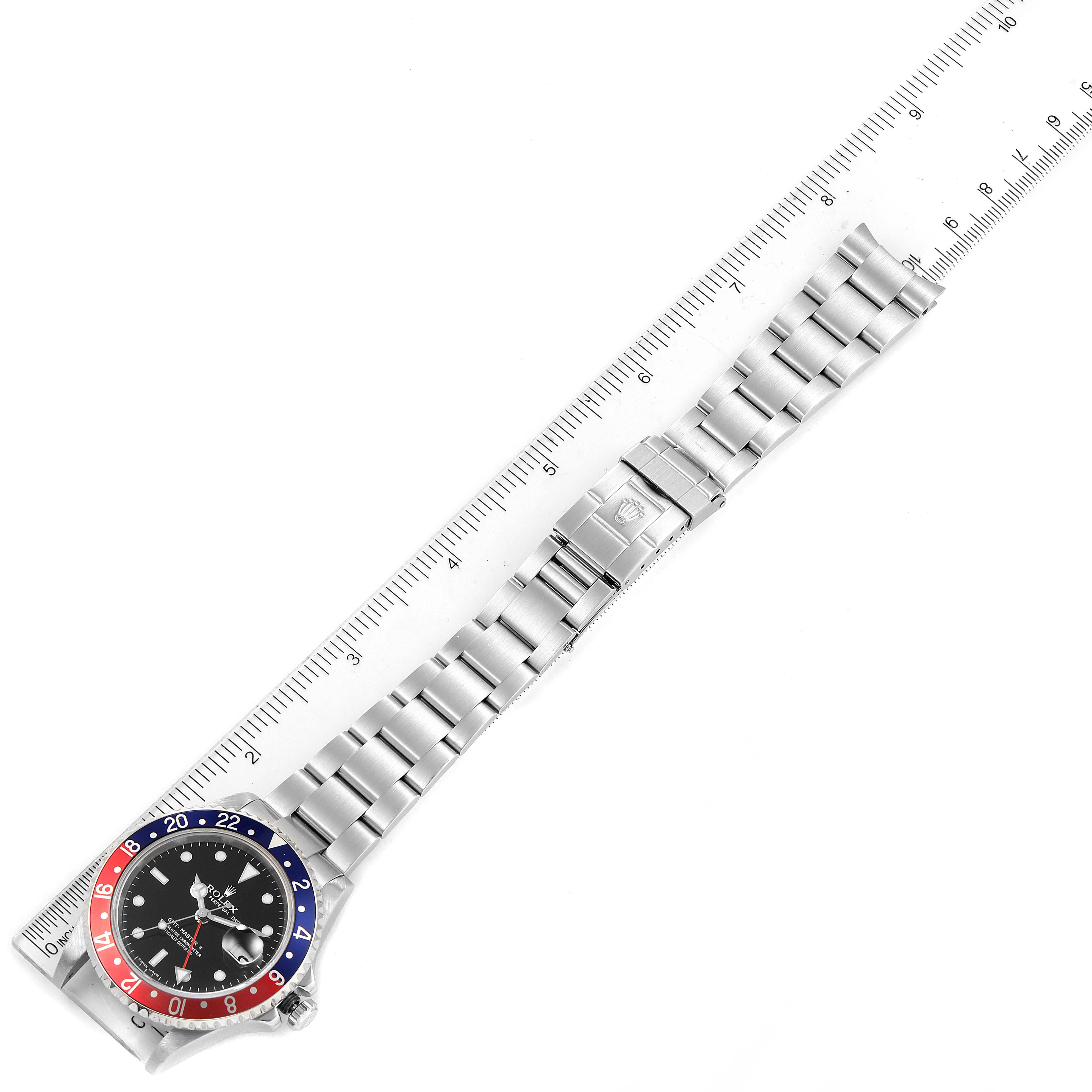 The image shows a top view of a Rolex GMT-Master 16710 Men
s Stainless Steel Black Dial 16710 Men
s Stainless Steel Black Dial watch, lying flat with a measuring scale beside it.
