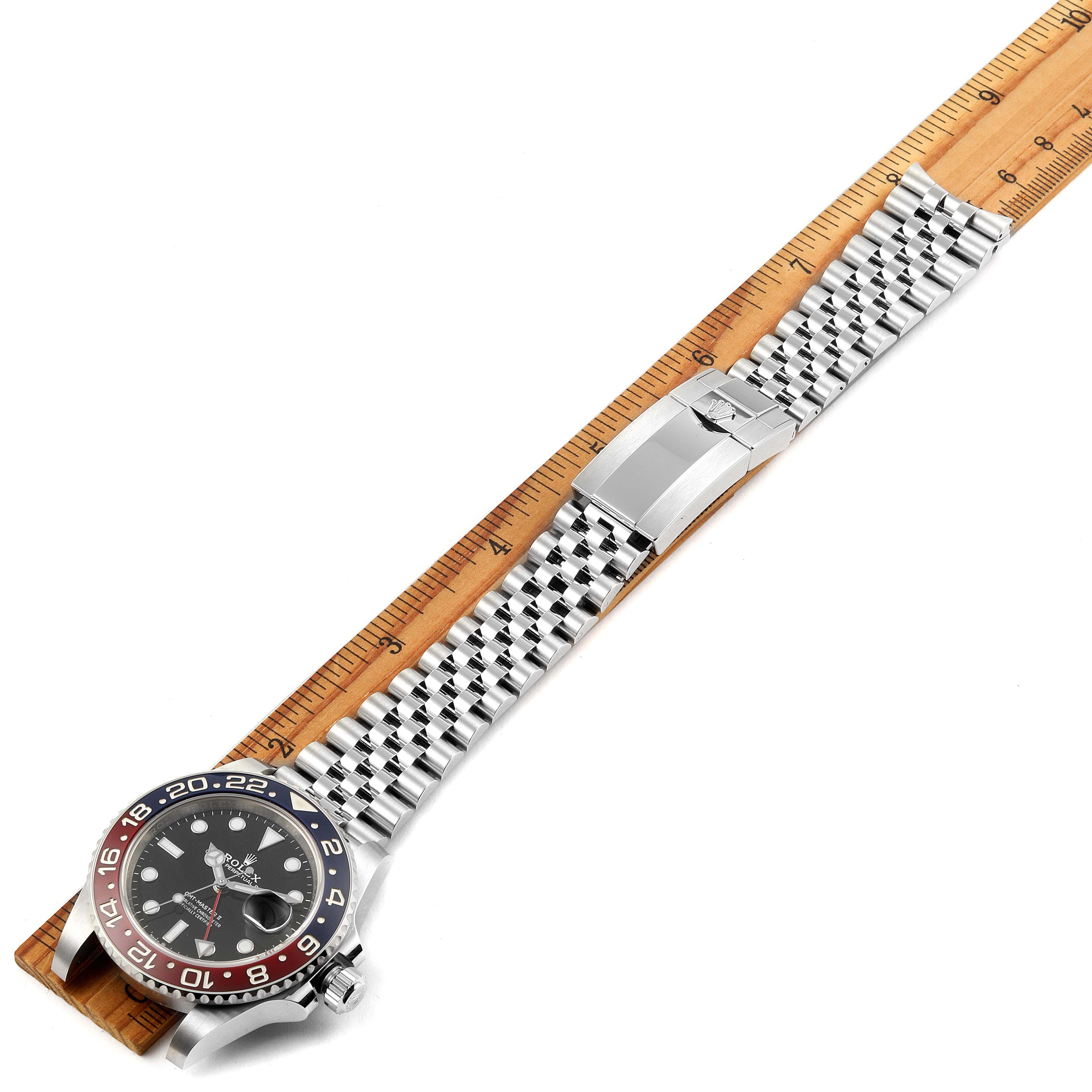 The Rolex GMT-Master 126710 Men
s Stainless Steel Black Dial 126710 Men
s Stainless Steel Black Dial watch is shown from a top-down angle, displaying the entire watch including the face, bezel, and bracelet laid next to a ruler.