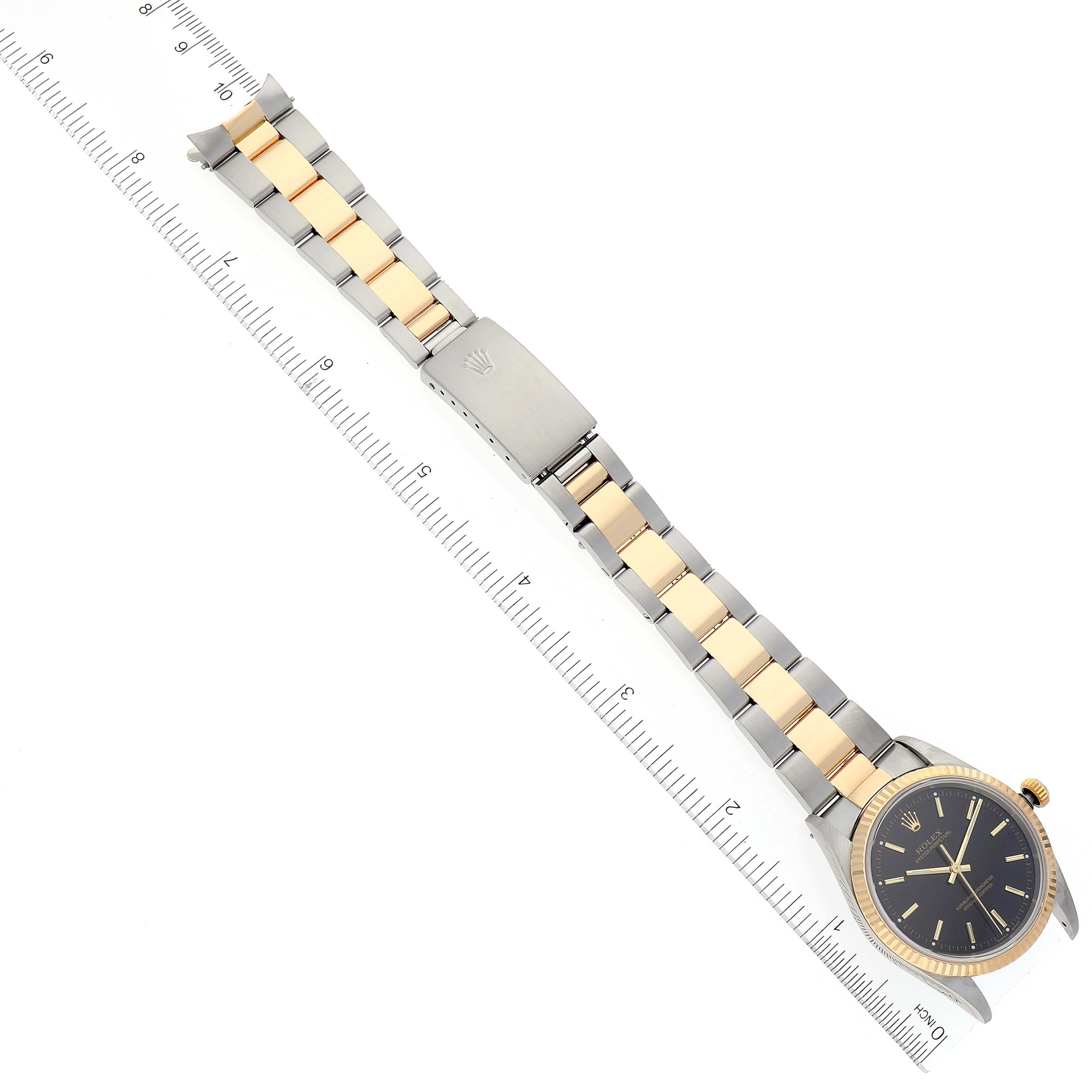 The image shows a full view of the Rolex Oyster Perpetual 14233 Men's Steel and Gold (two tone) Black Dial 14233 Men's Steel and Gold (two tone) Black Dial watch, including its face and metal bracelet laid next to a ruler.