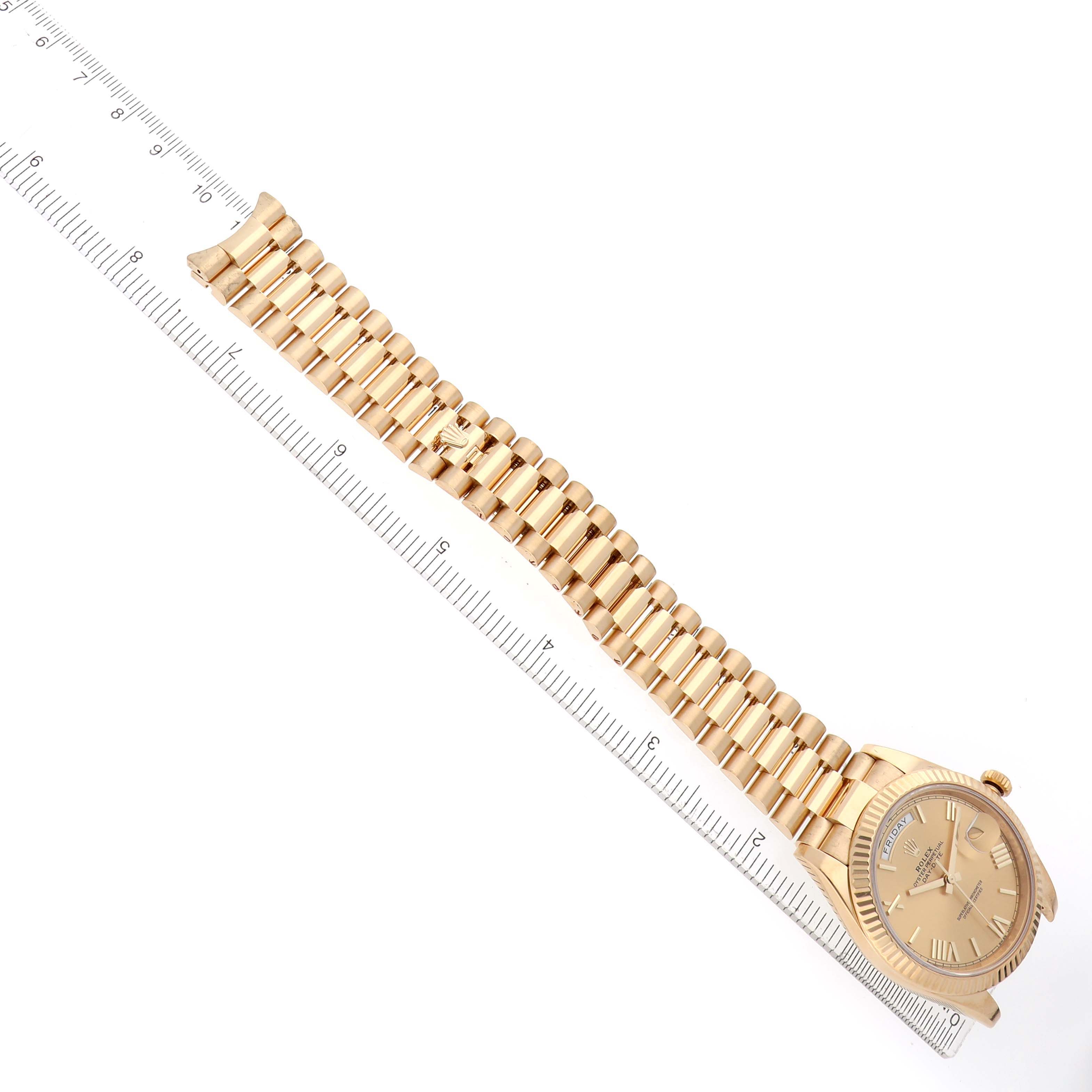 The Rolex President 228238 Men's Yellow Gold Champagne Dial watch is shown at an angled top view, highlighting the bracelet, case, and face next to a ruler.