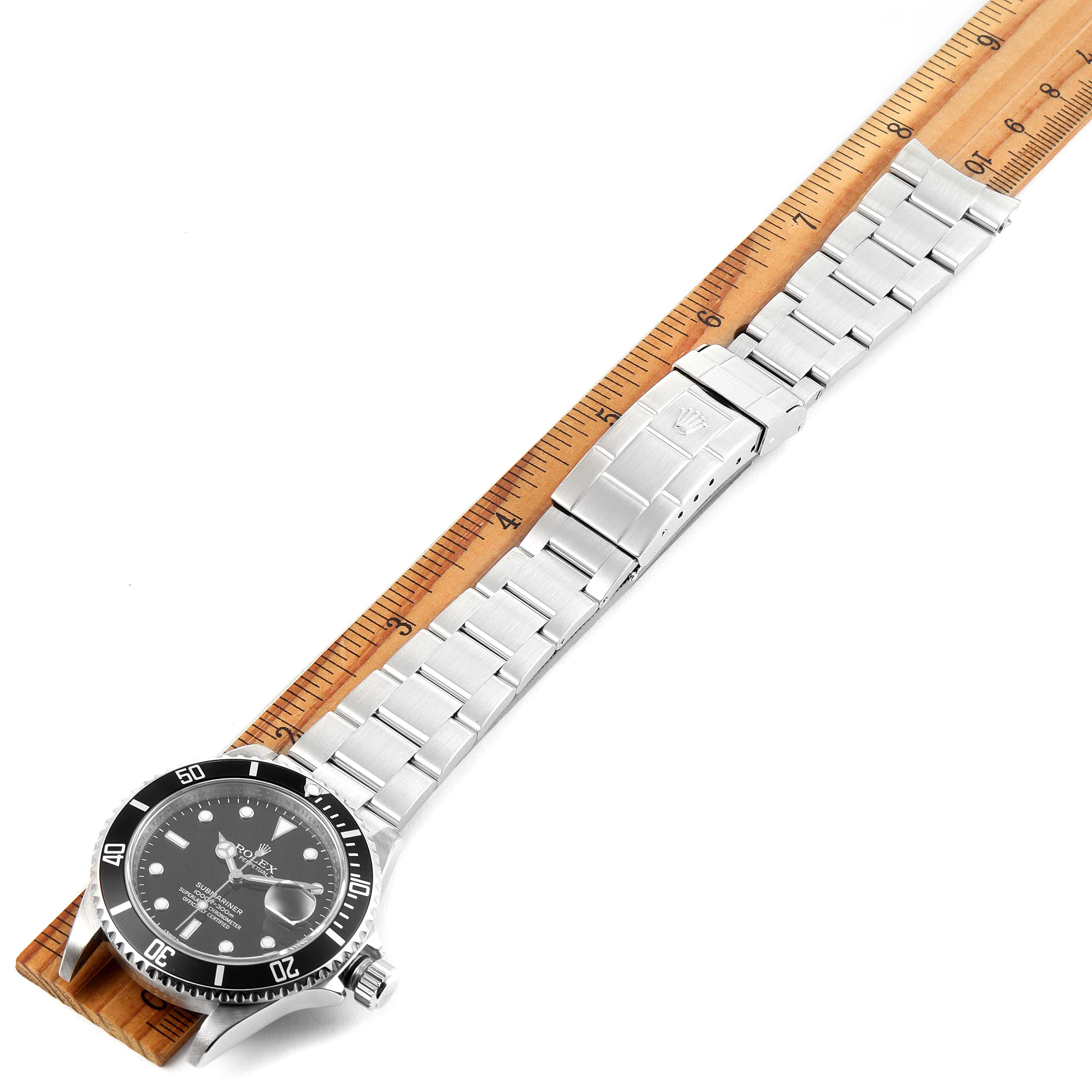 The image shows a Rolex Submariner 16610 Men
s Stainless Steel Black Dial 16610 Men
s Stainless Steel Black Dial watch laid flat with a metal bracelet alongside a wooden ruler for size reference.