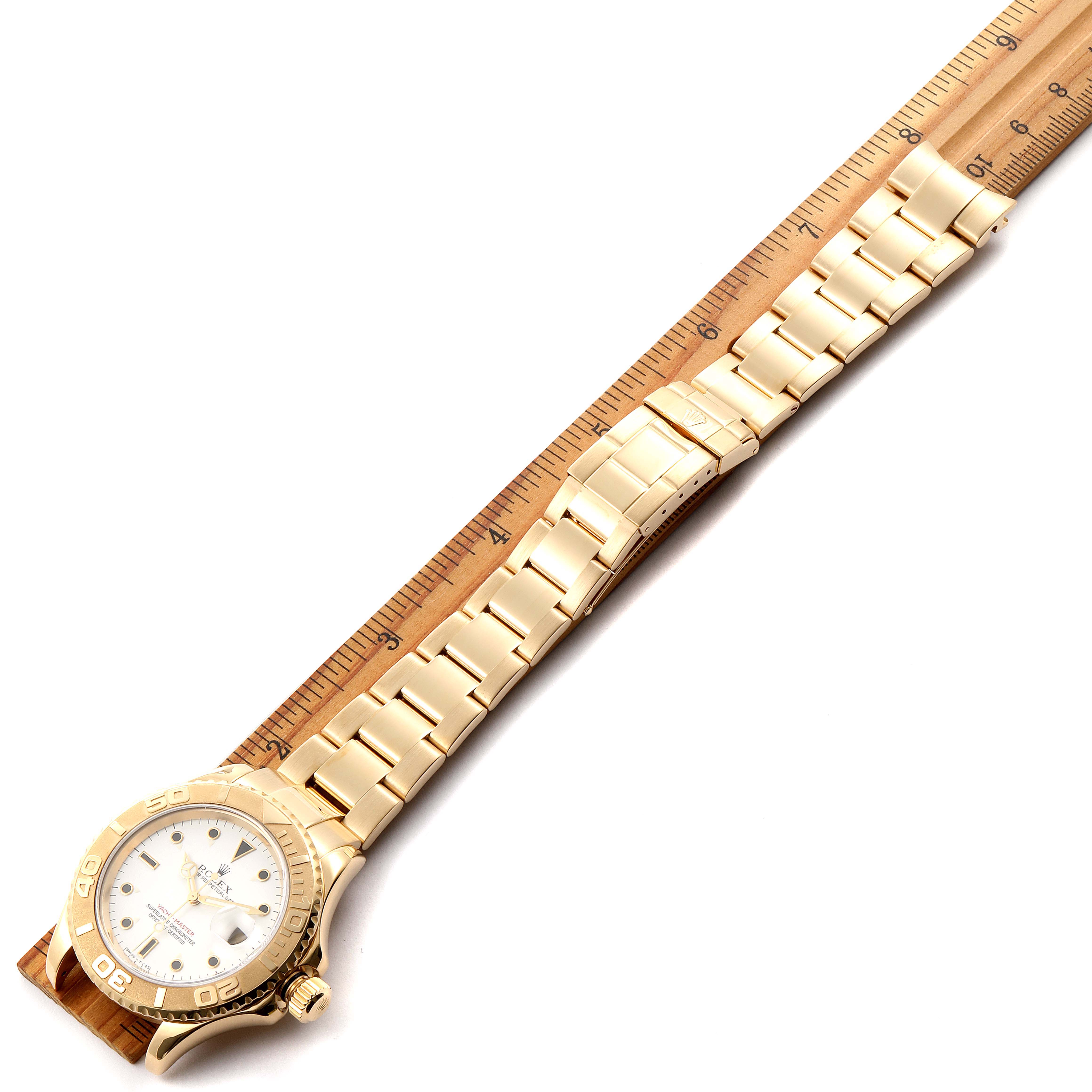 The image shows a Rolex Yacht-Master 16628 Men's Yellow Gold White Dial 16628 Men's Yellow Gold White Dial watch at an angle, highlighting its face, bezel, and full bracelet alongside a measuring ruler.