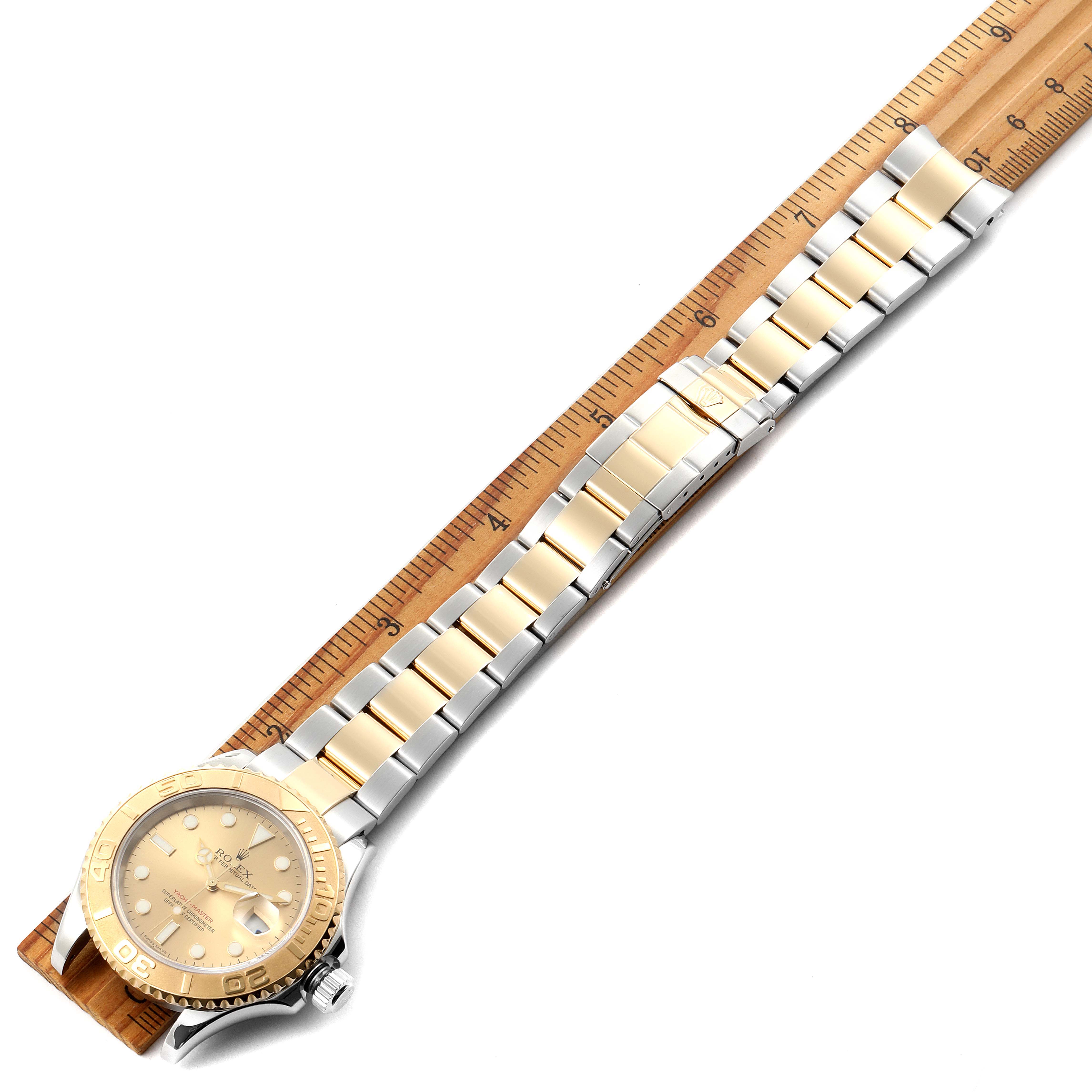 The image shows a Yacht-Master model by Rolex placed diagonally across a wooden ruler.
