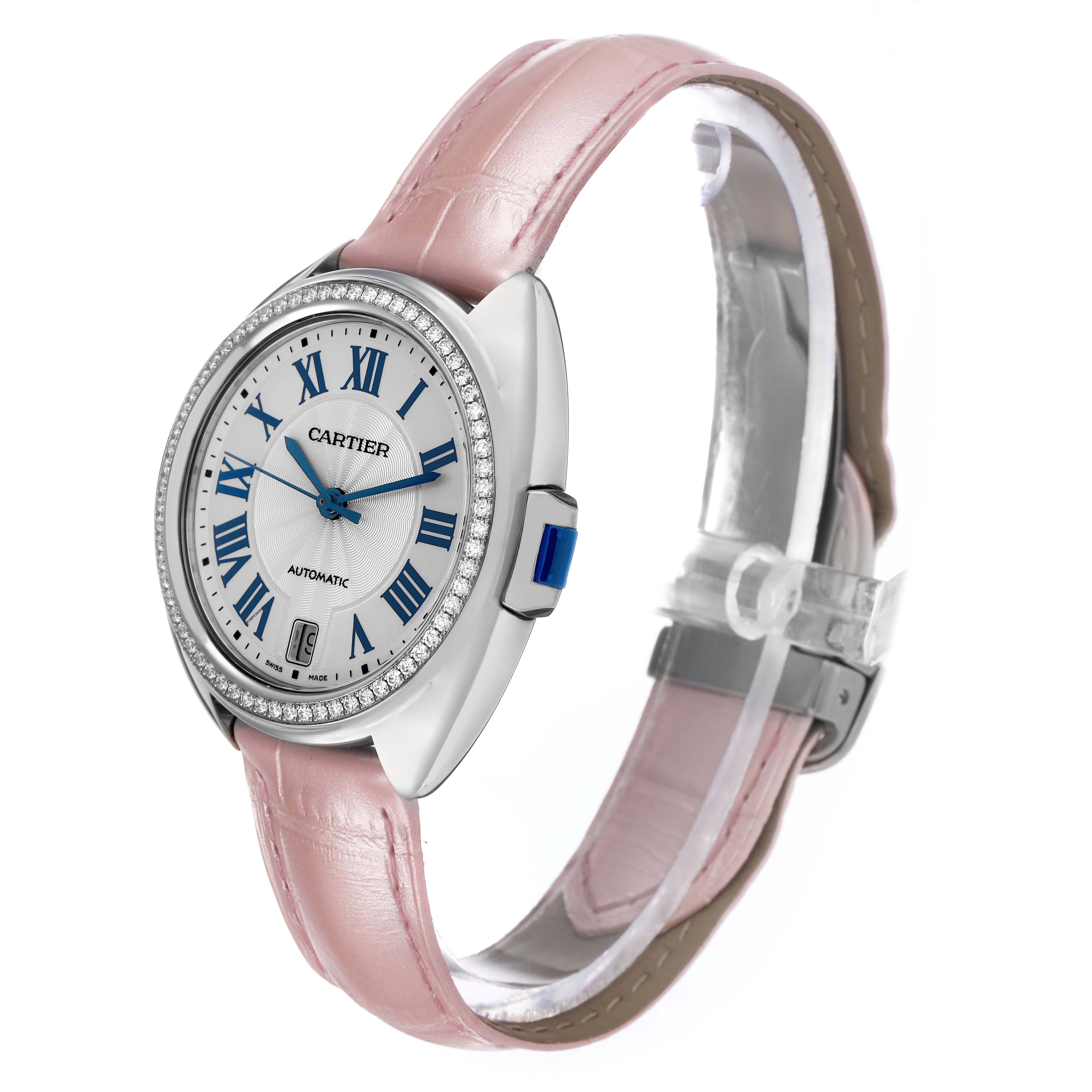The Cartier Clé watch is shown at a three-quarter angle featuring a pink leather strap, diamond bezel, and blue hands on the dial.