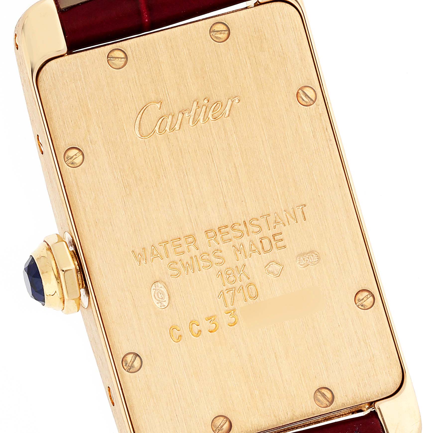 This image shows the back case of a Cartier Tank Americaine W2601556 Women
s Yellow Gold Silver Dial W2601556 Women
s Yellow Gold Silver Dial watch, displaying engravings and the crown with a gemstone.