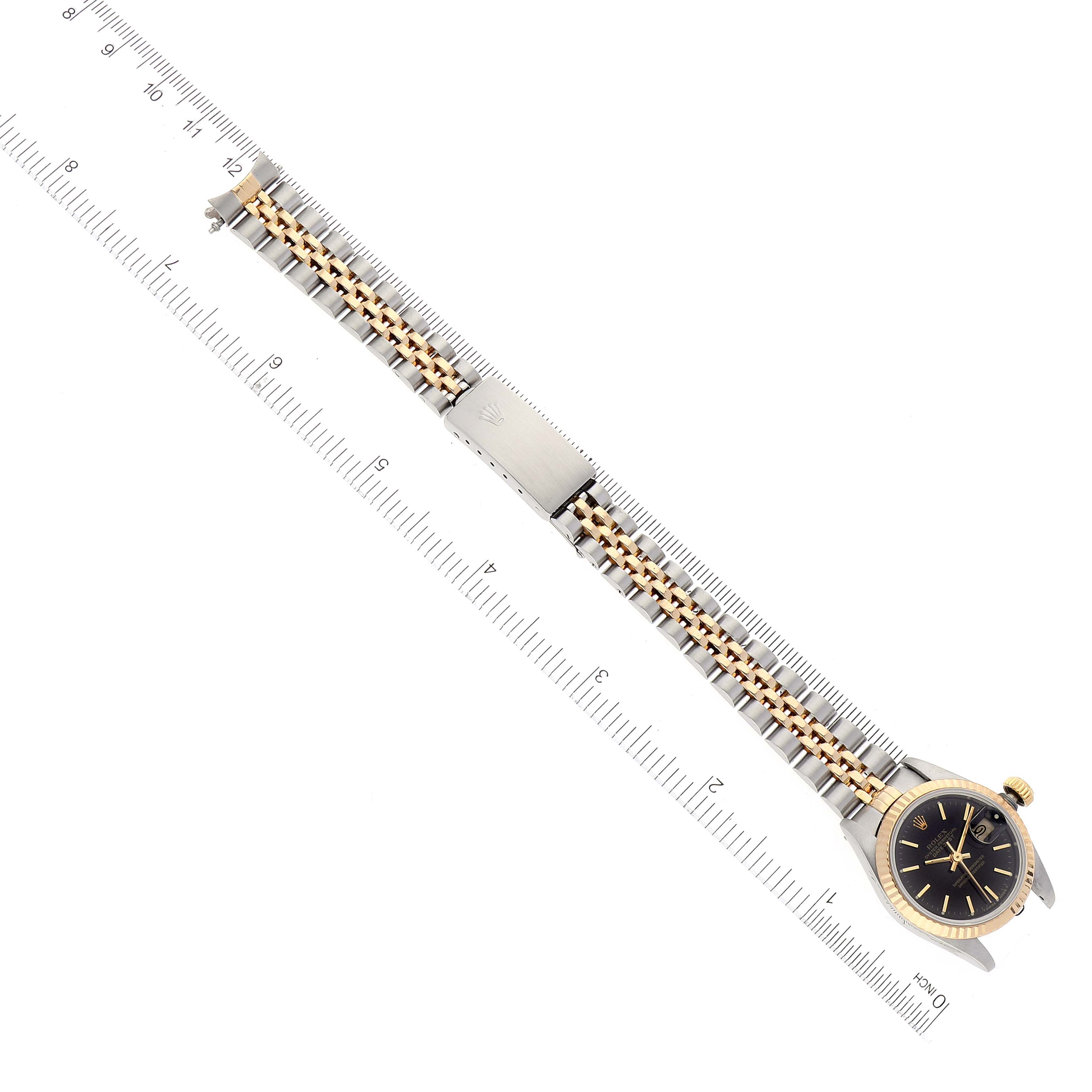The image shows a Rolex Datejust 69173 Women's Steel and Gold (two tone) Black Dial 69173 Women's Steel and Gold (two tone) Black Dial watch with a ruler for scale, highlighting its two-tone bracelet and black dial from a top-down angle.