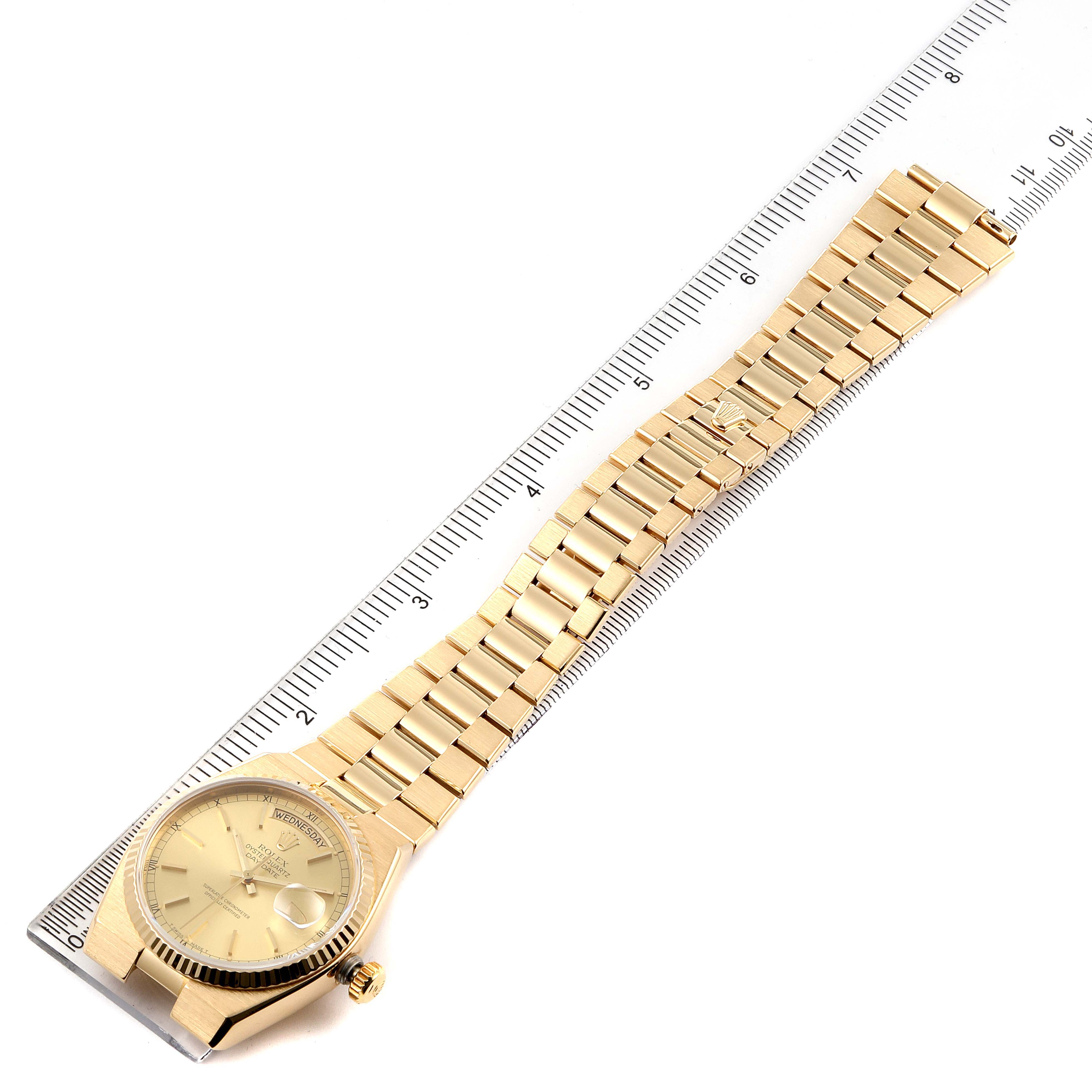 The Rolex Oysterquartz 19018 Men's Yellow Gold Champagne Dial 19018 Men's Yellow Gold Champagne Dial watch is shown laid flat alongside a ruler, displaying its face, bracelet, and clasp.